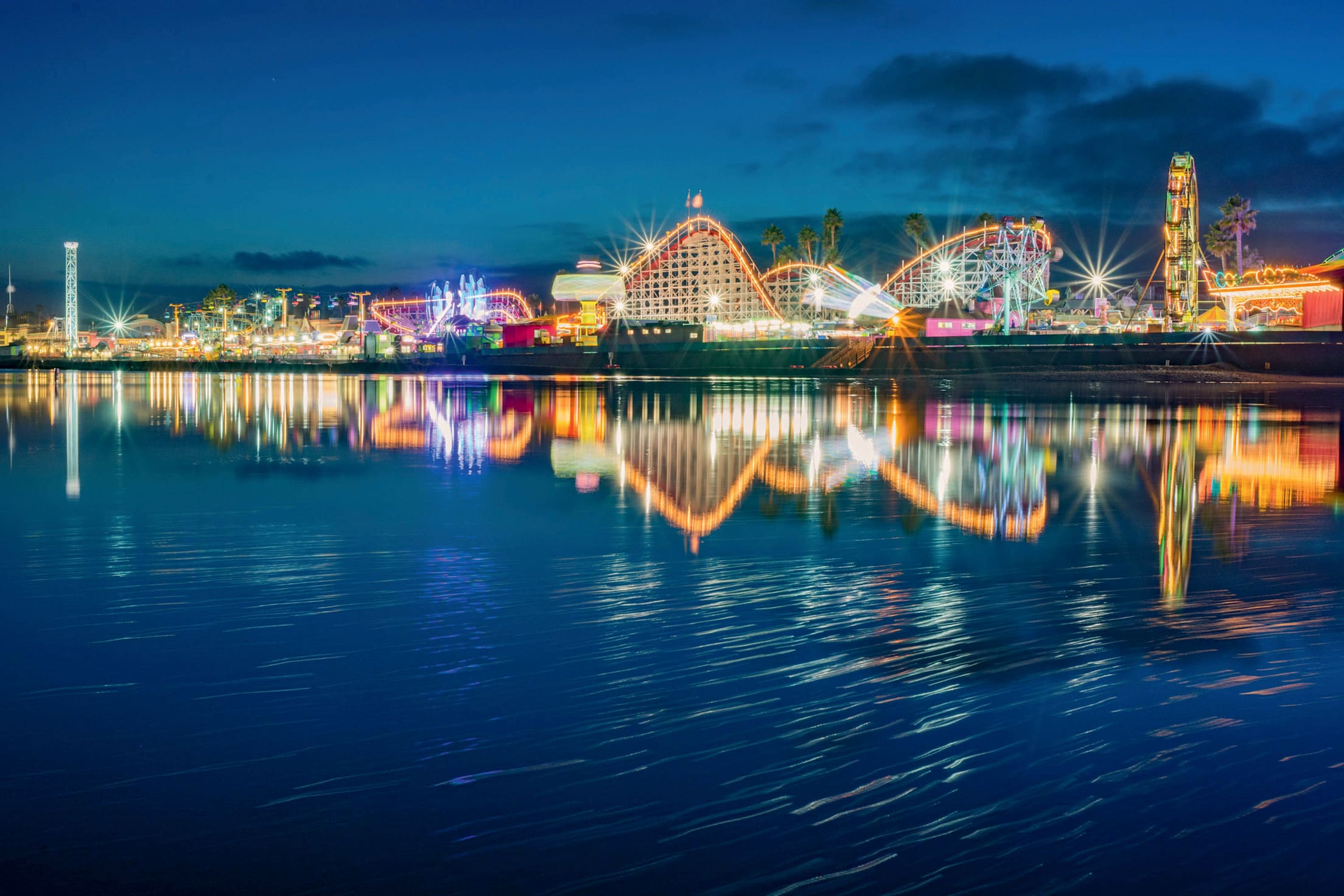 Lights from the Santa Cruz Beach Boardwalk reflecting across the ocean at night.