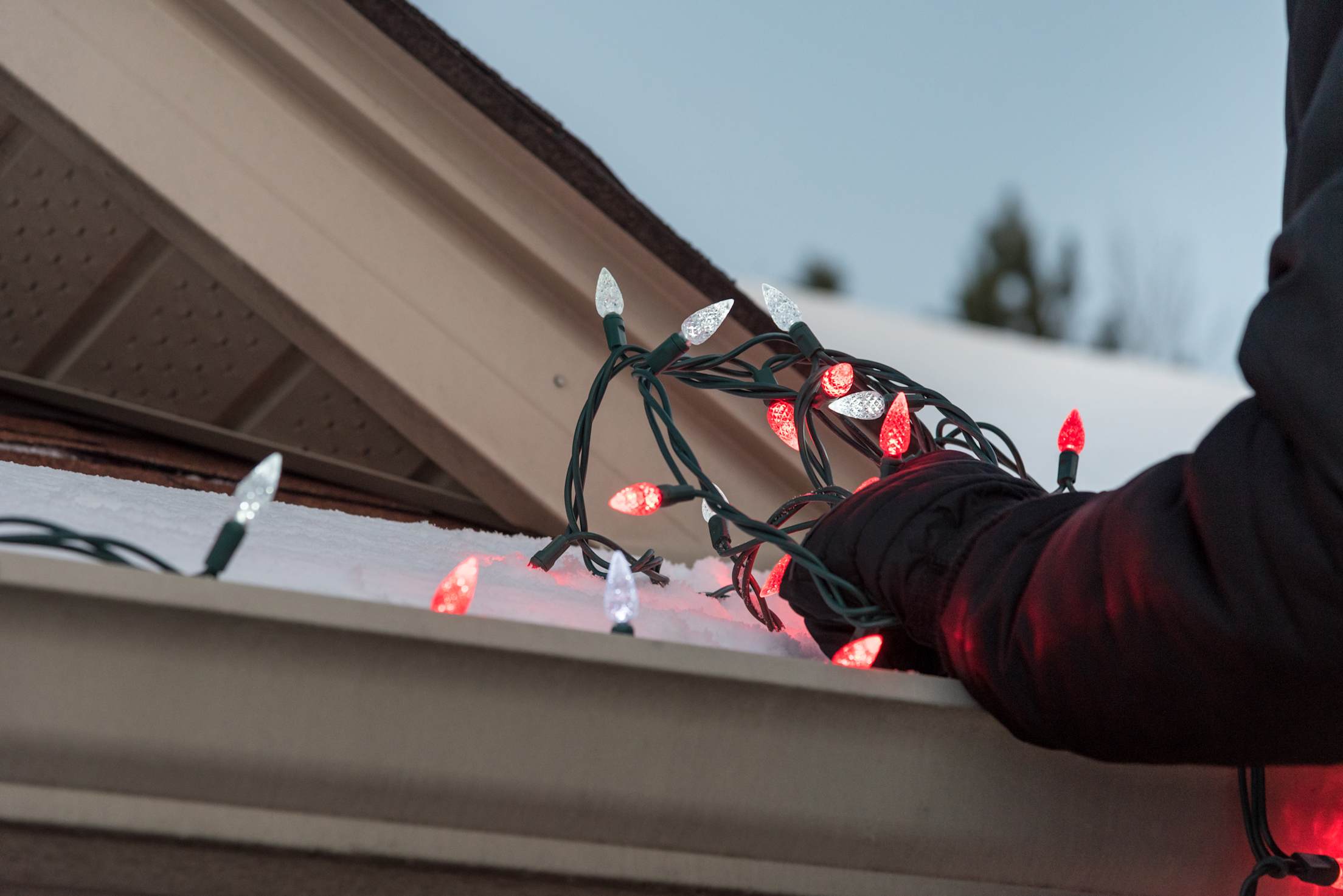 A person puts up multi-colored LED string lights on their porch.