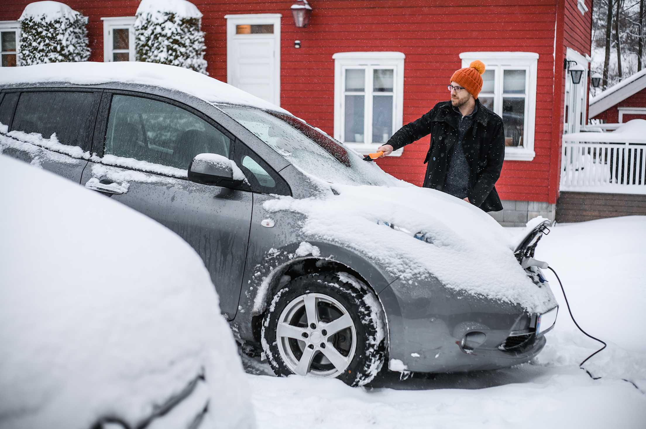 A driver removes snow and ice from their electric car.