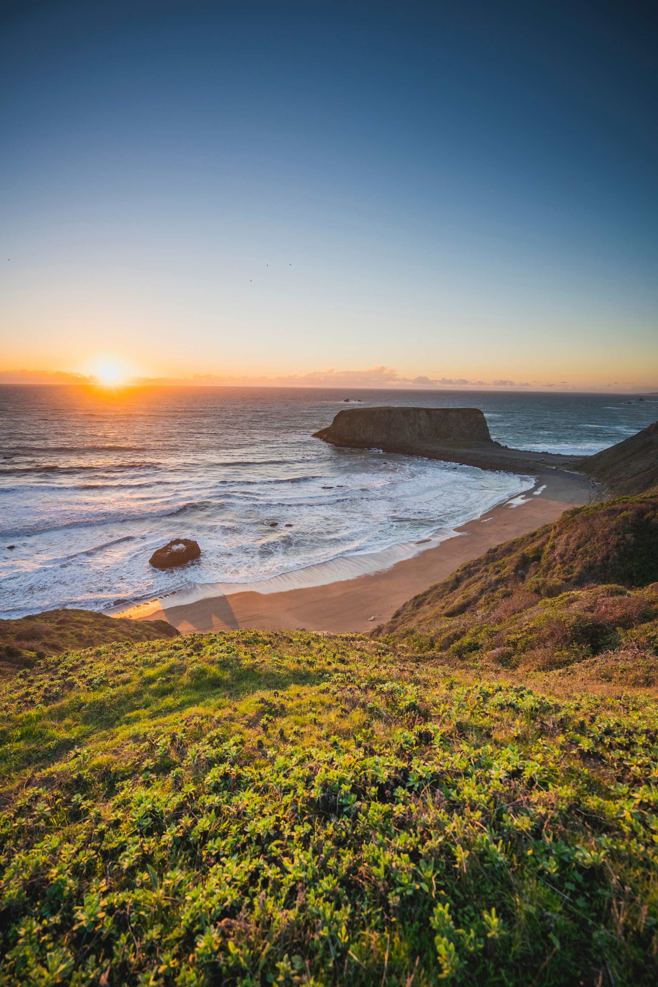 The sun sets behind white waves in Goat Rock State Park.
