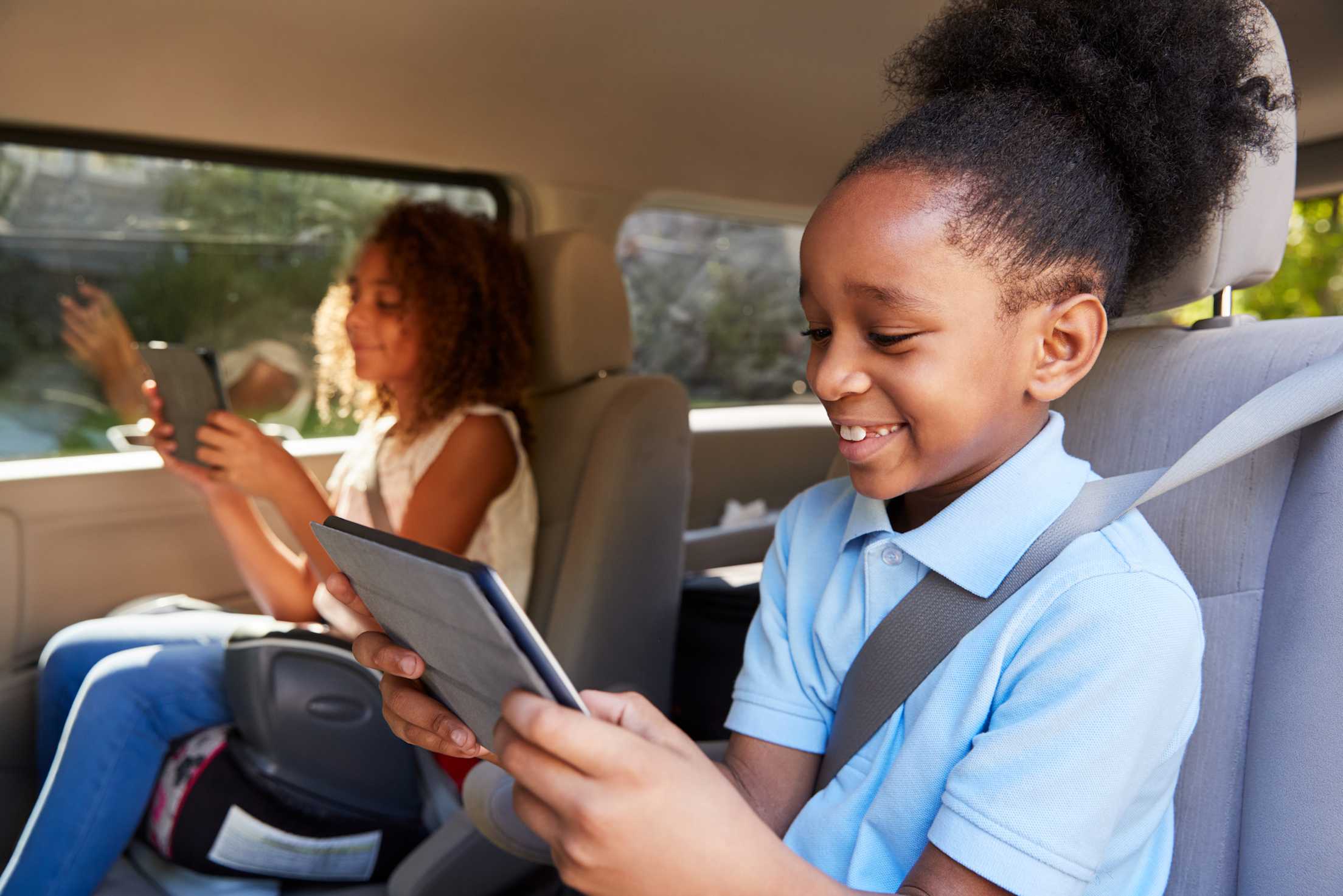 picture of two young girls in the backseat of a car looking at tablets