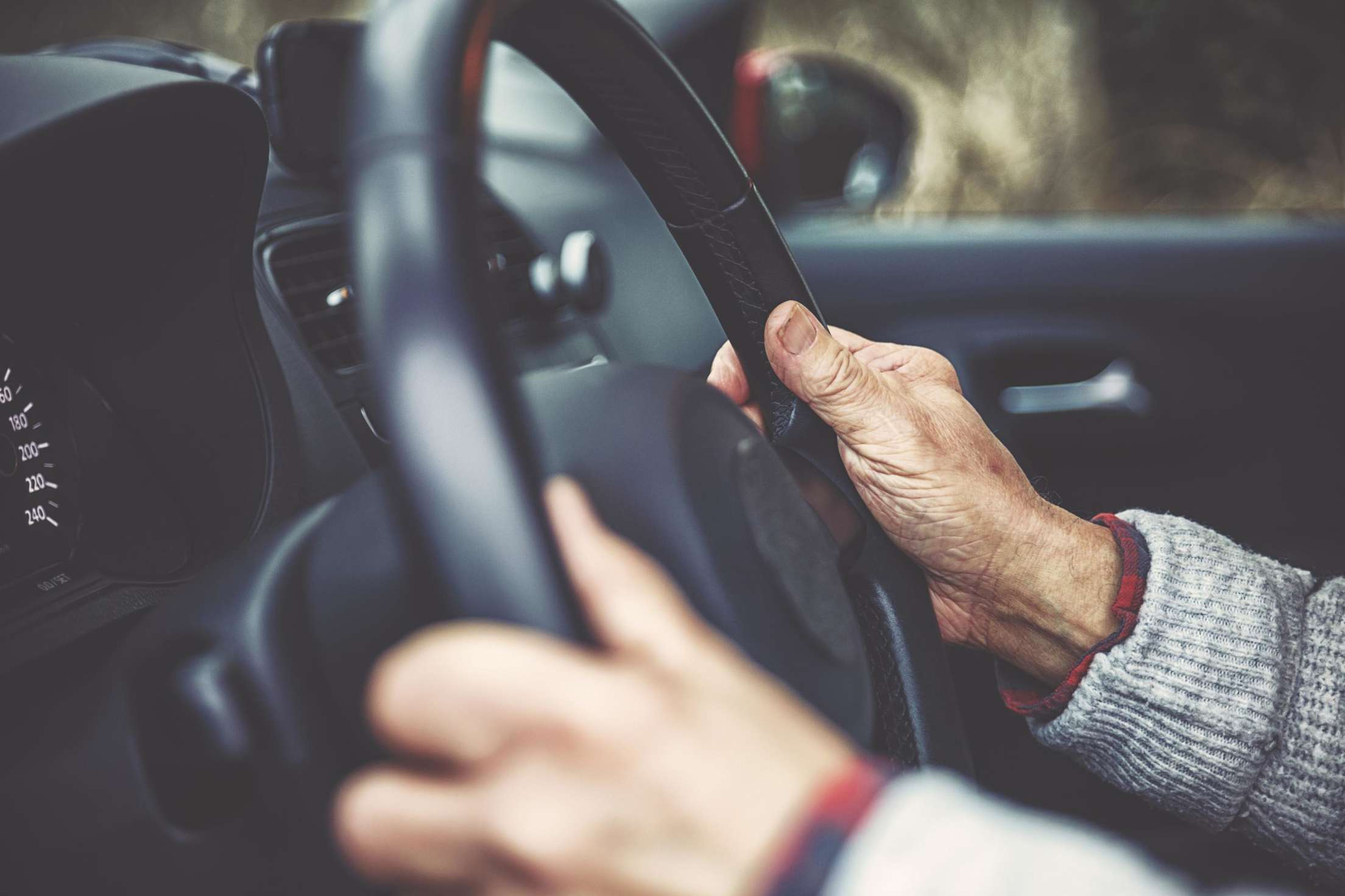 An older woman holds a steering wheel at 3 and 9 o'clock.