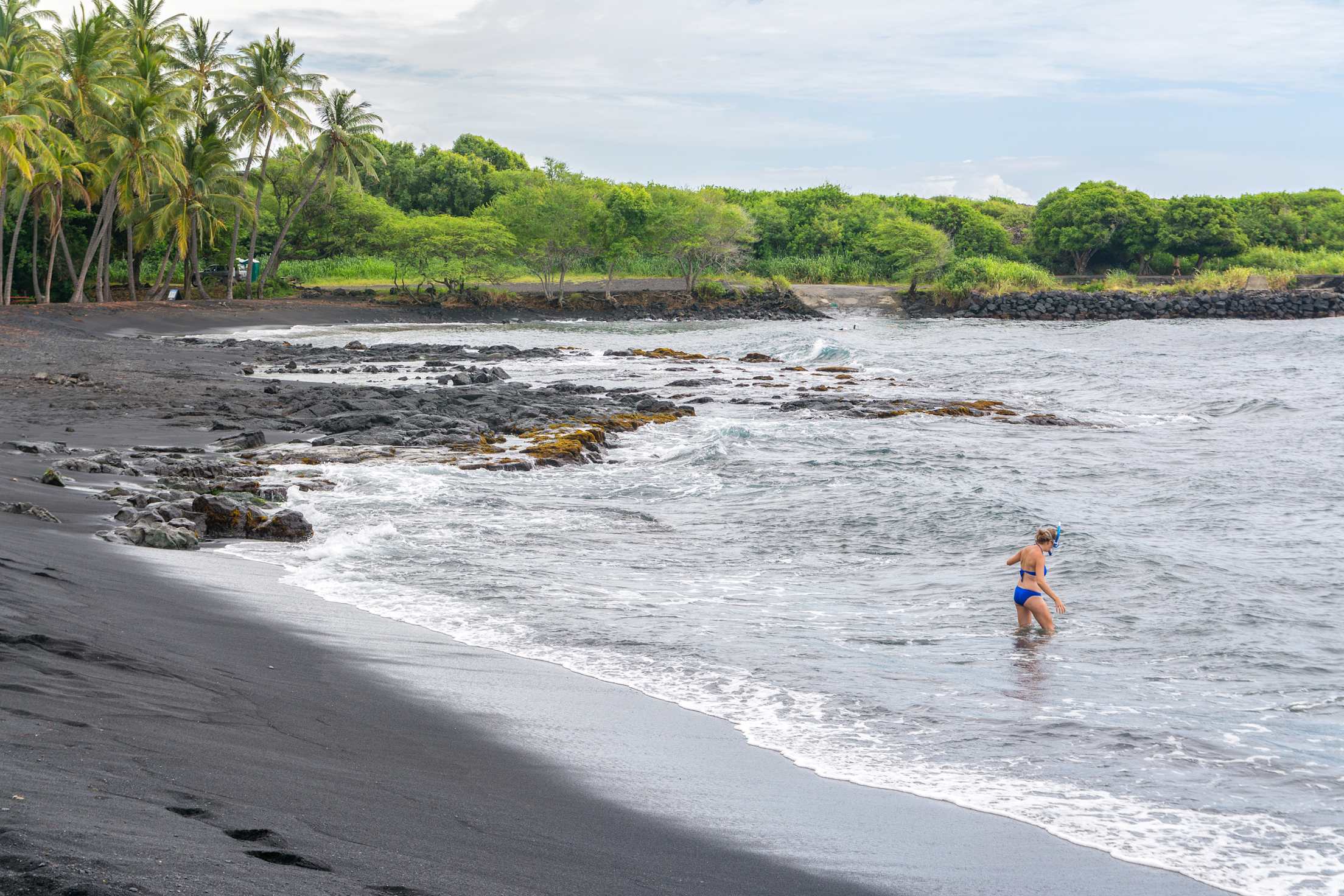 A woman walks into the waves with her snorkle at Punalu'u Black Sand Beach Park.