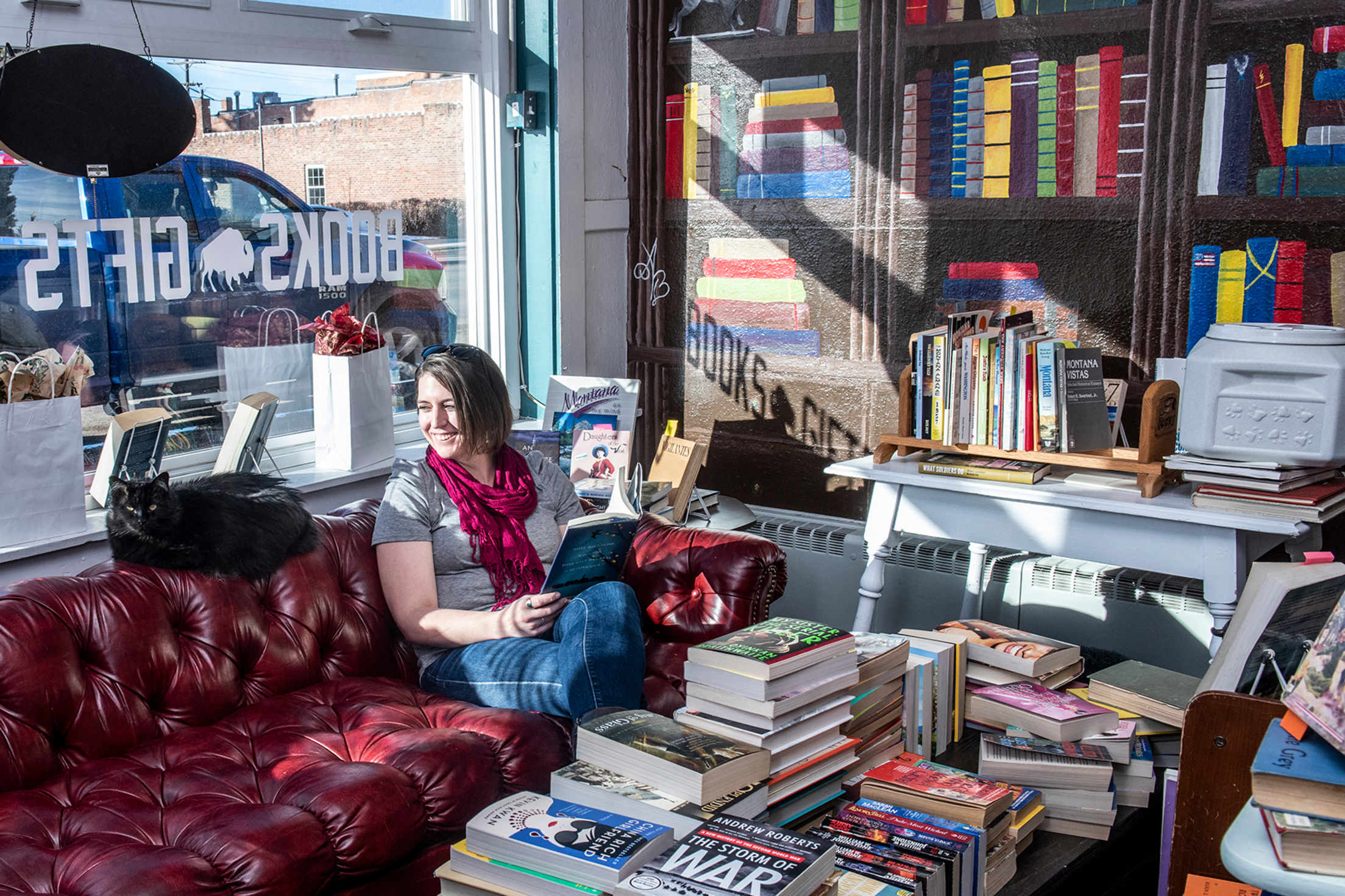A woman sits on the couch with the shop cat at Browsing Bison in Deer Lodge, Montana.