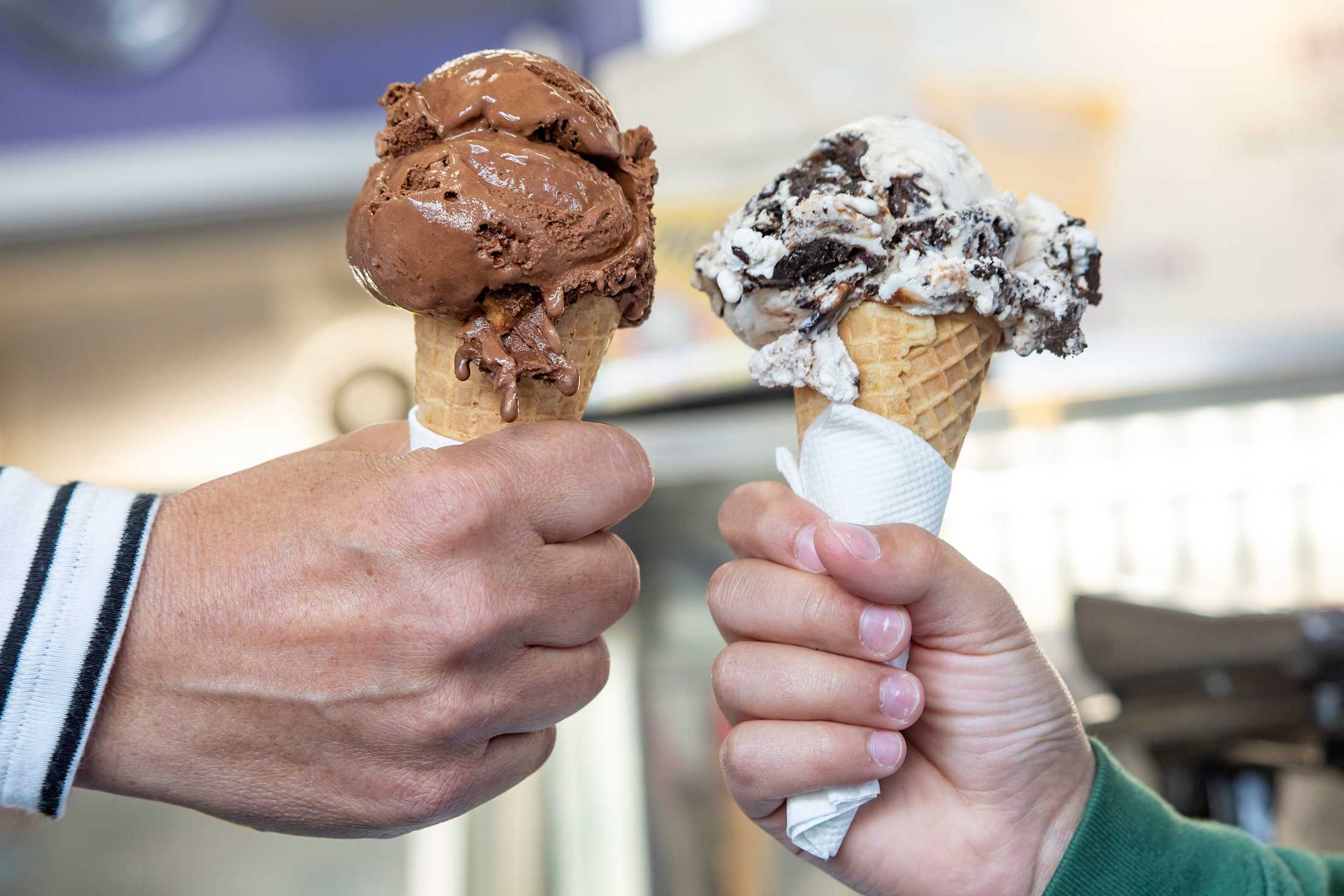 Two customers hold scoops of chocolate caramel crackle and Oreo cookie in cones from Mitchell’s Ice Cream in San Francisco.