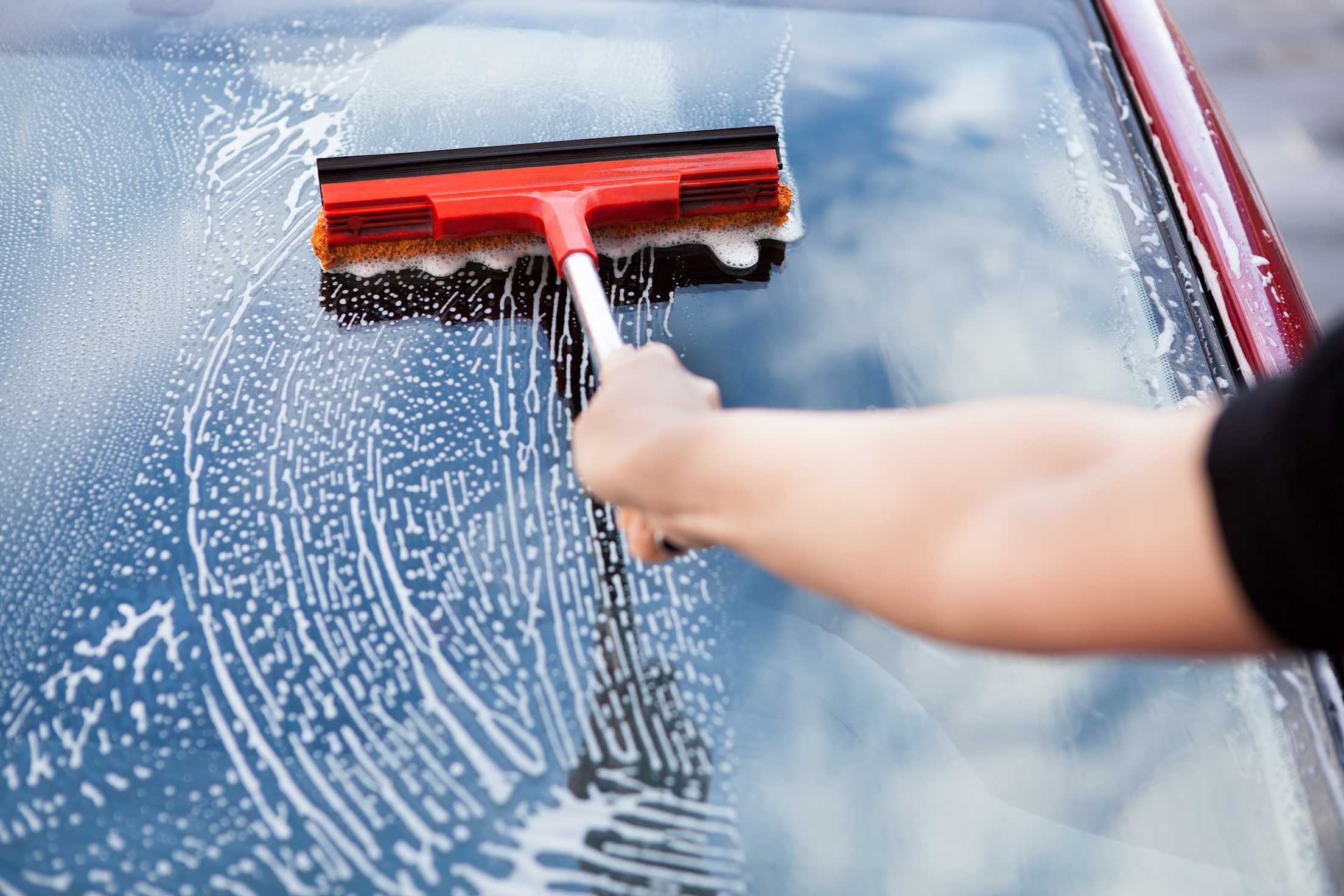 A driver cleans their windshield at a gas station.
