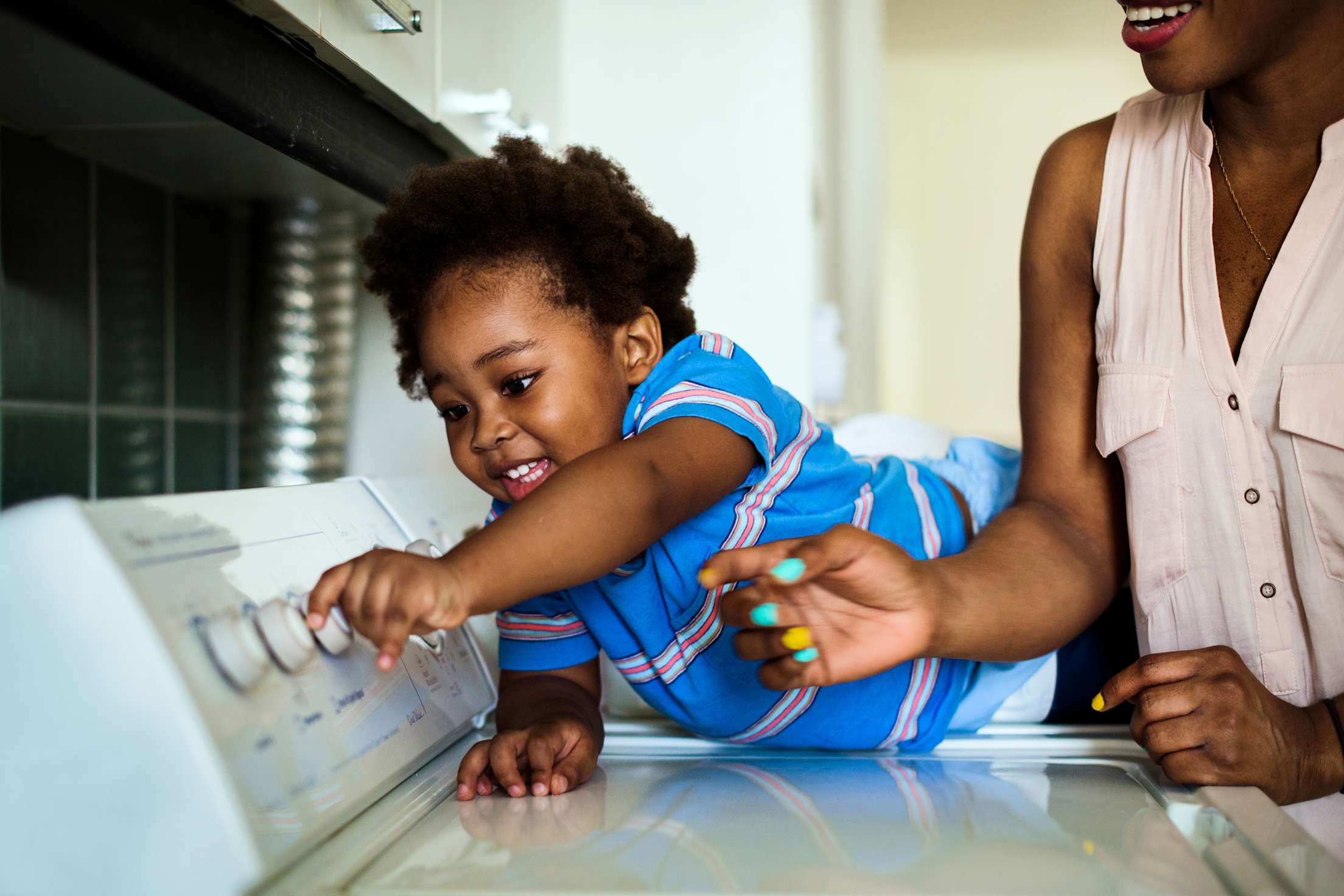 A child helps their mom start the washing machine.