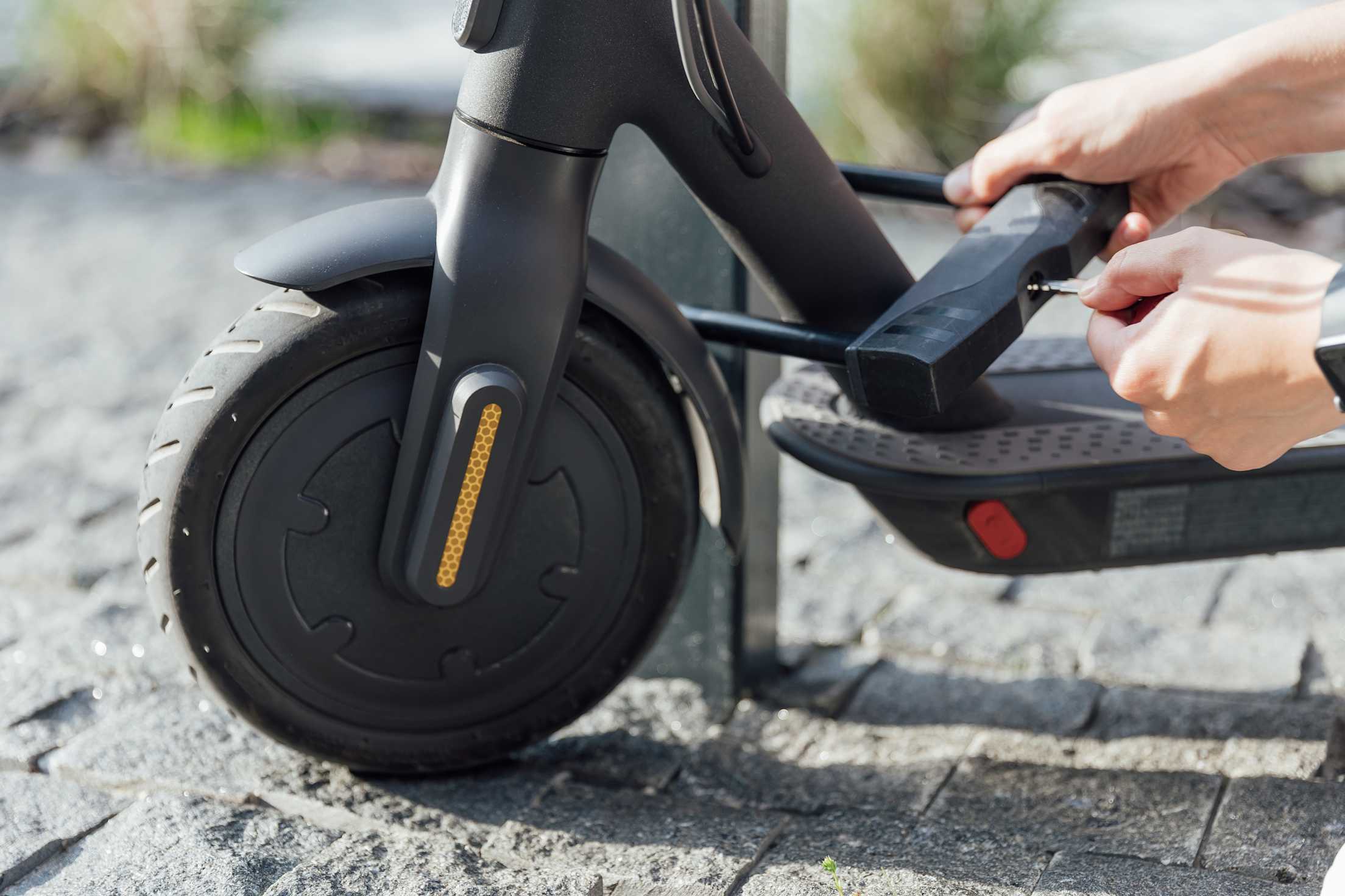 A person locks their electric scooter with a u-lock to a bike rack.