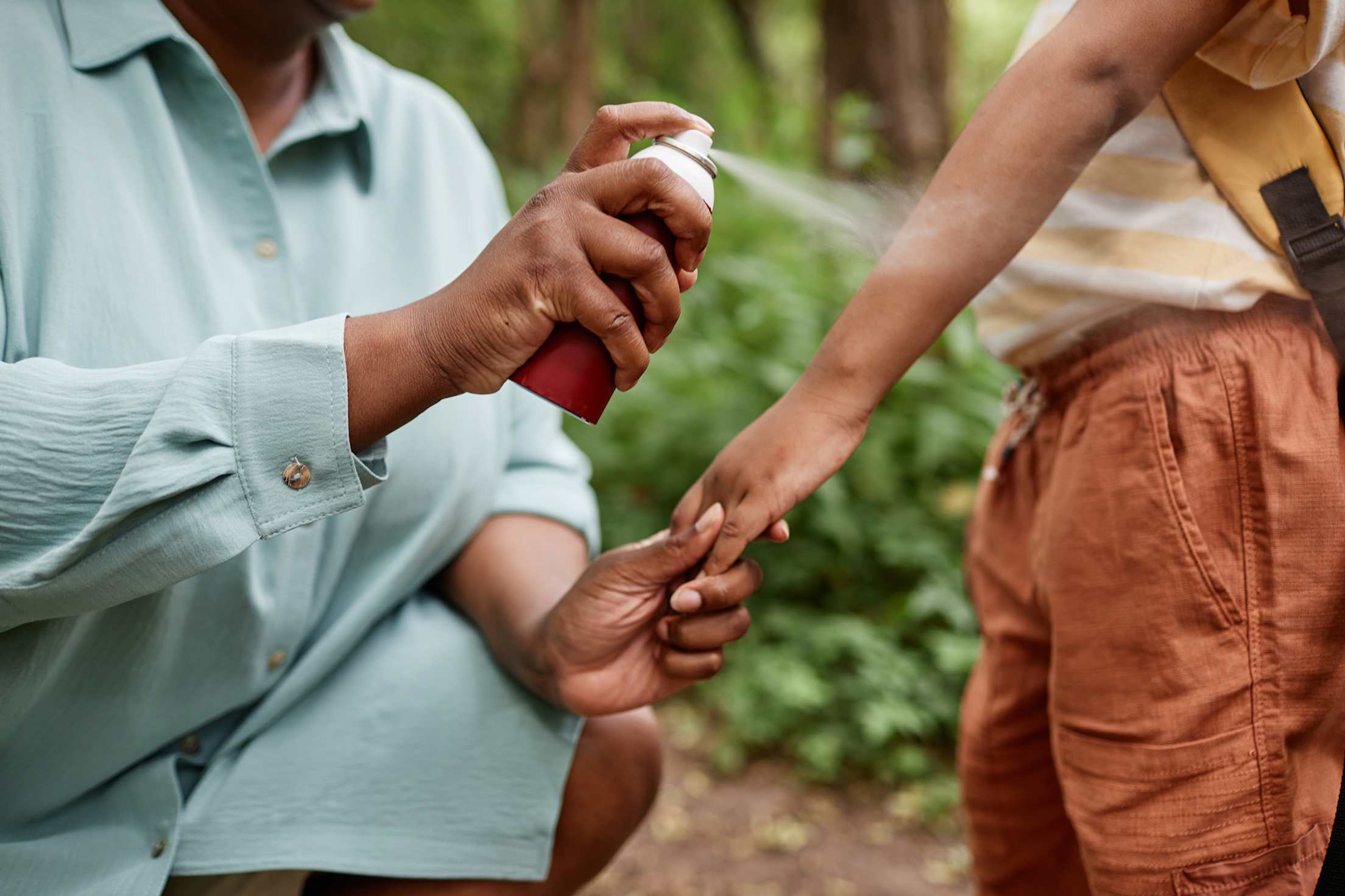 A parent applies bug spray to their child before going on a hike.