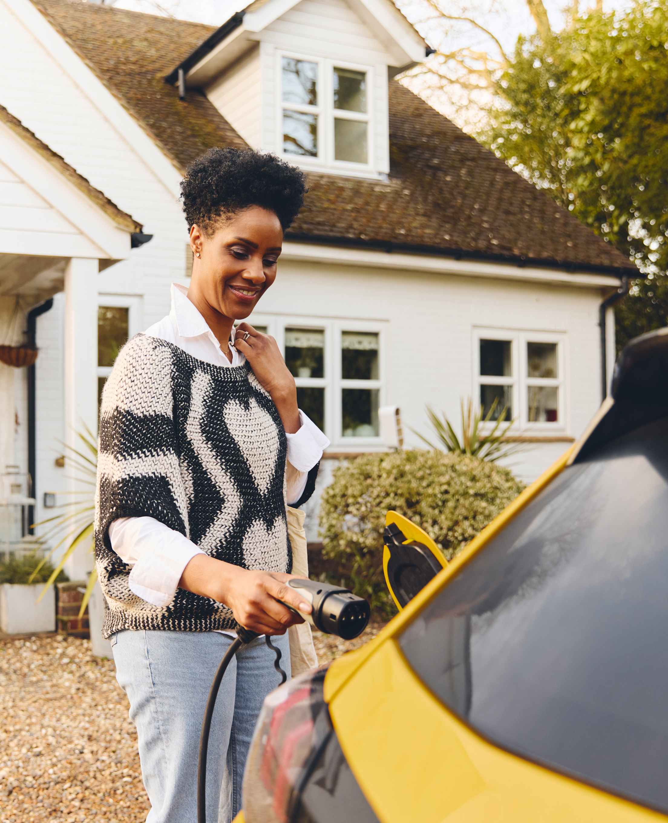 A woman plugs in her yellow EV to charge.