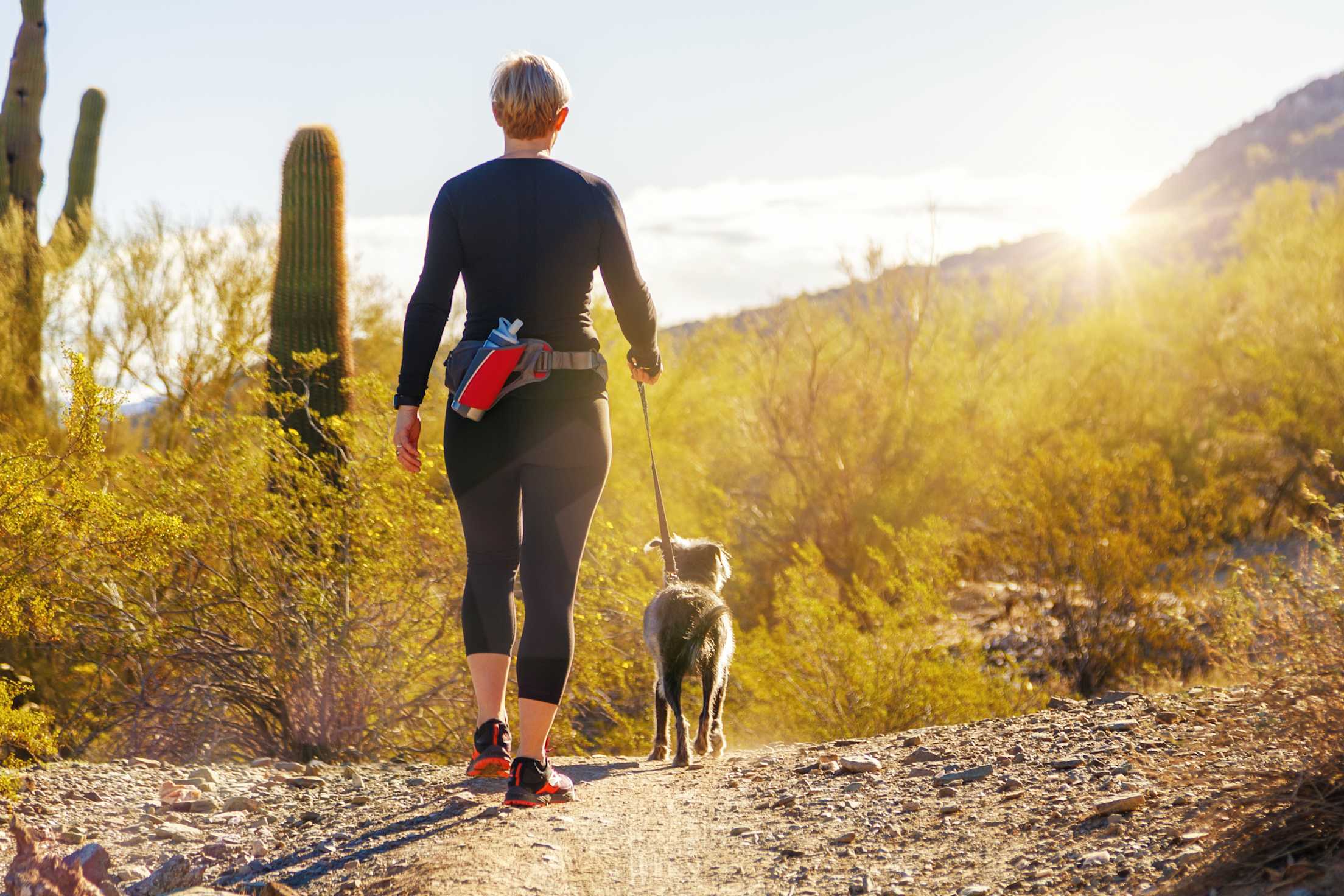 A woman hikes in the desert with her dog.