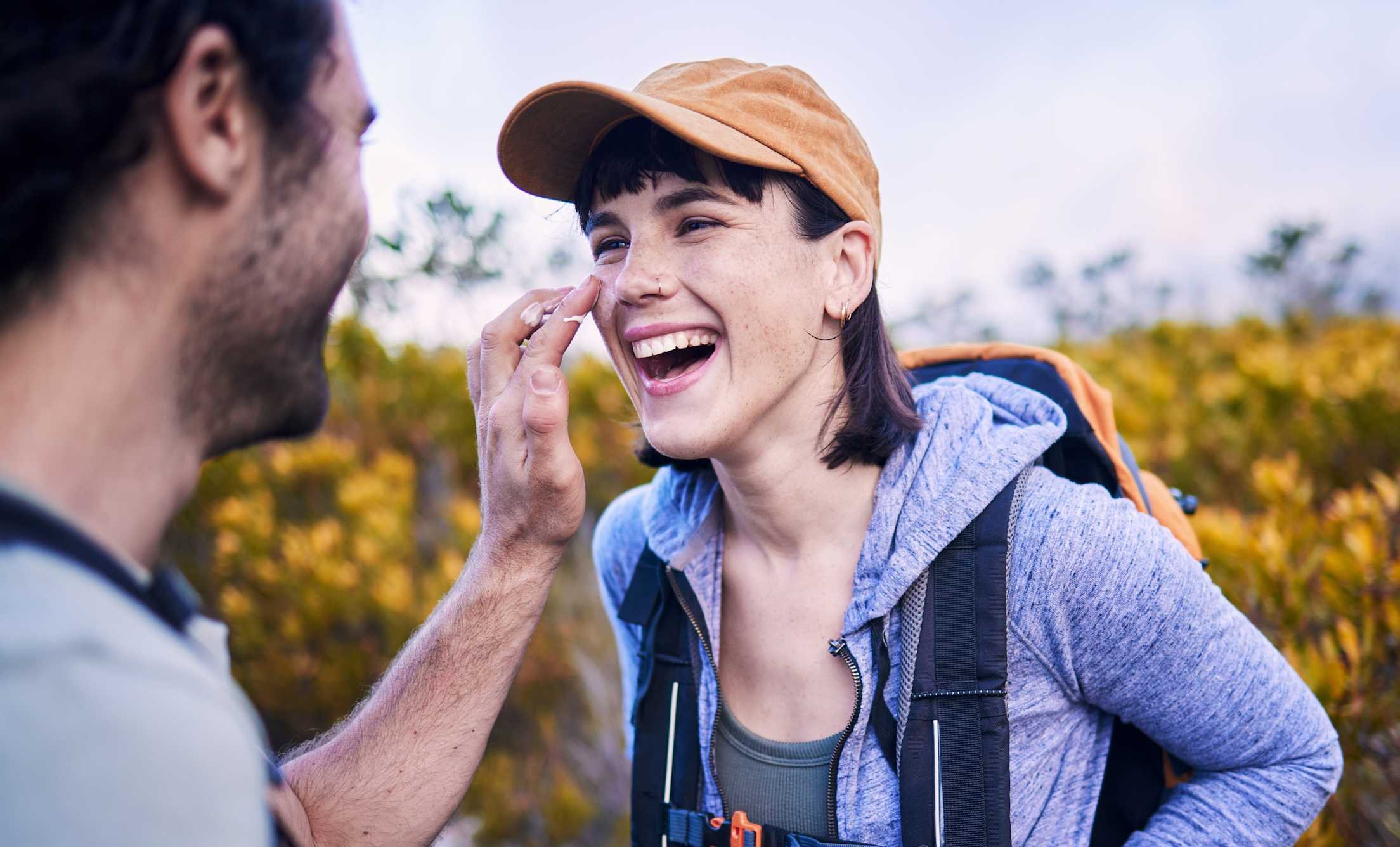 A man applies sunscreen to his partner's face out on a trail.