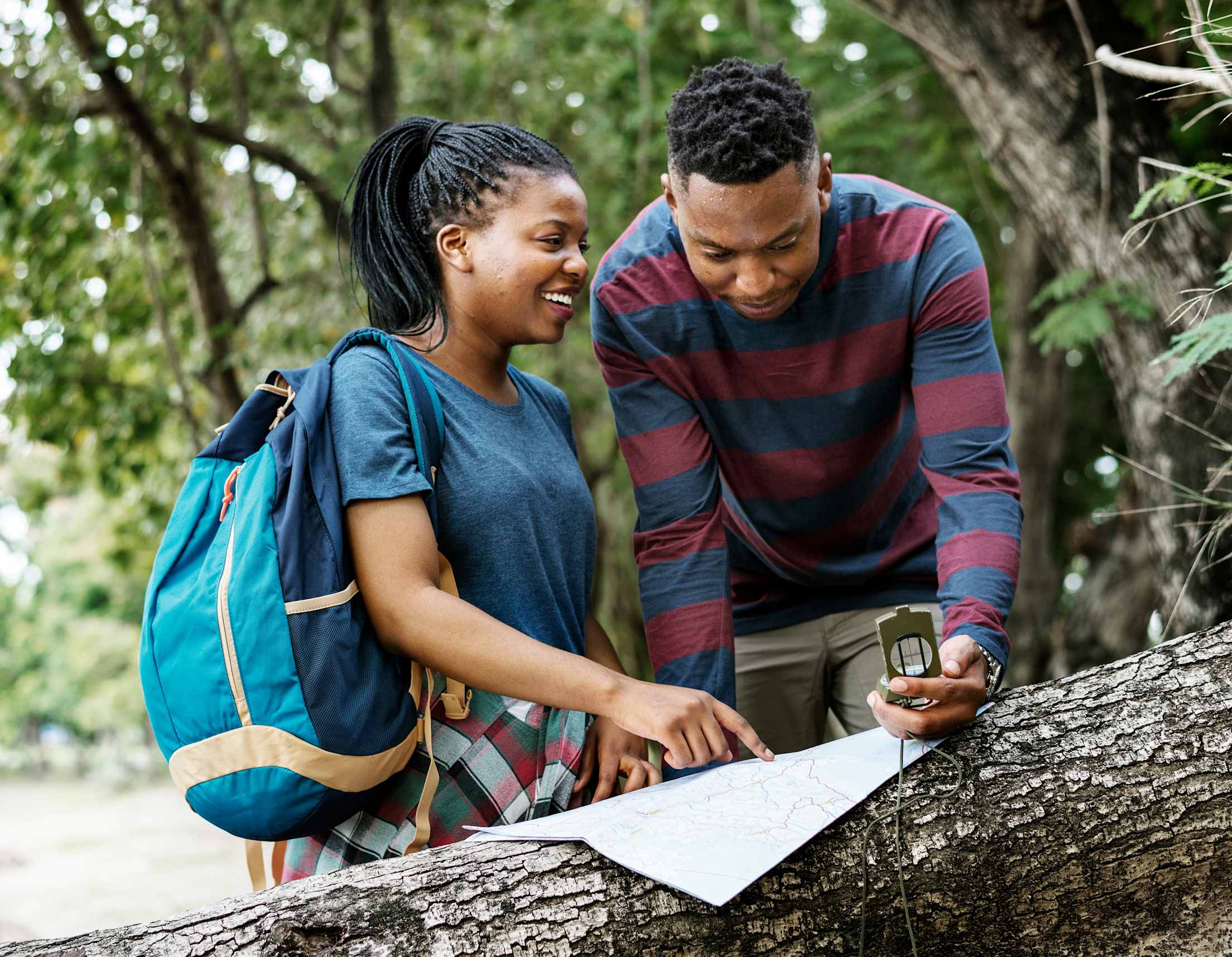 Two hikers use their map and compass to navigate on a forest trail.