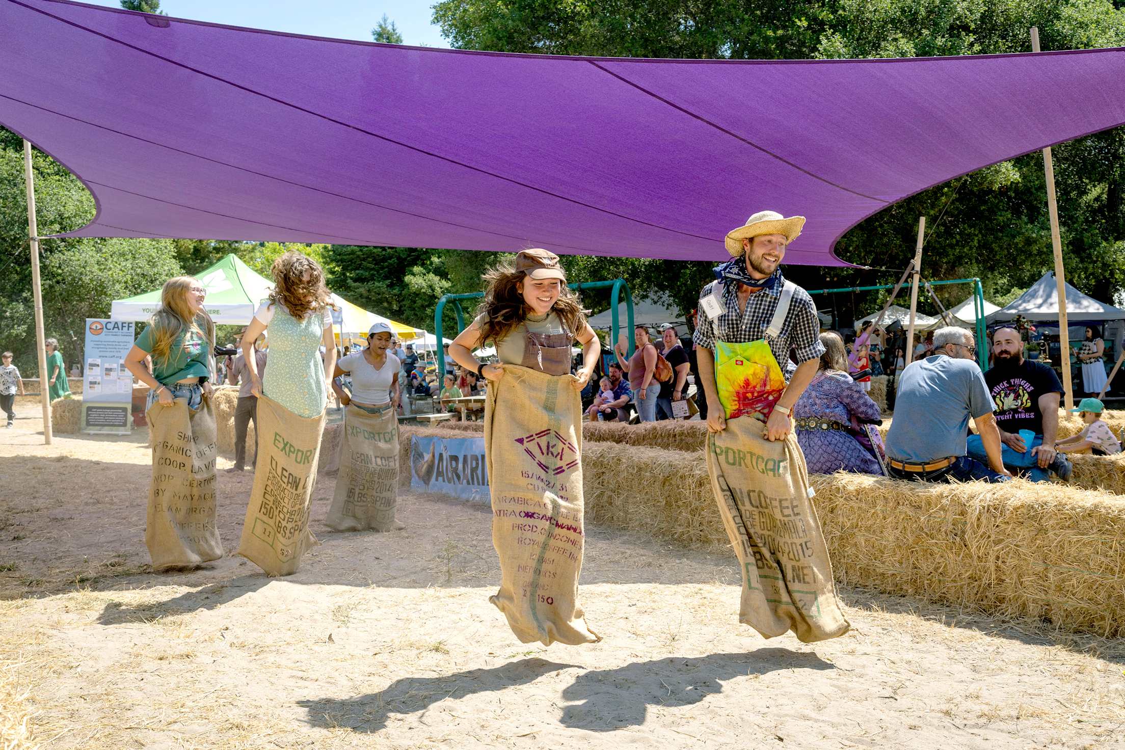 A group of adults and teens compete in a sack race.