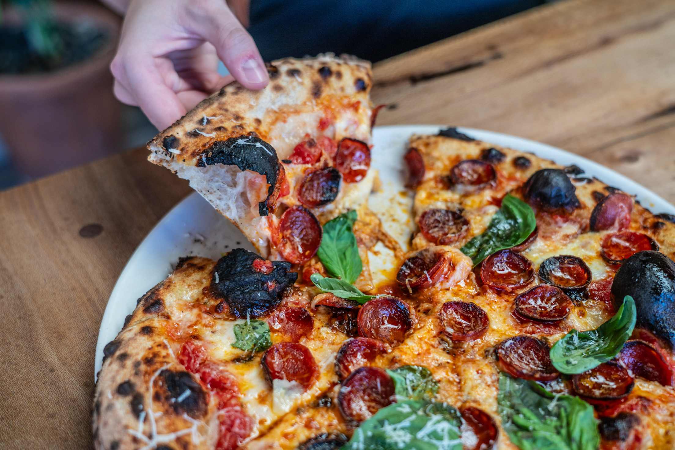A person removes a slice of a Dos Cabezas WineWorks' wood-fired pepperoni pizza.