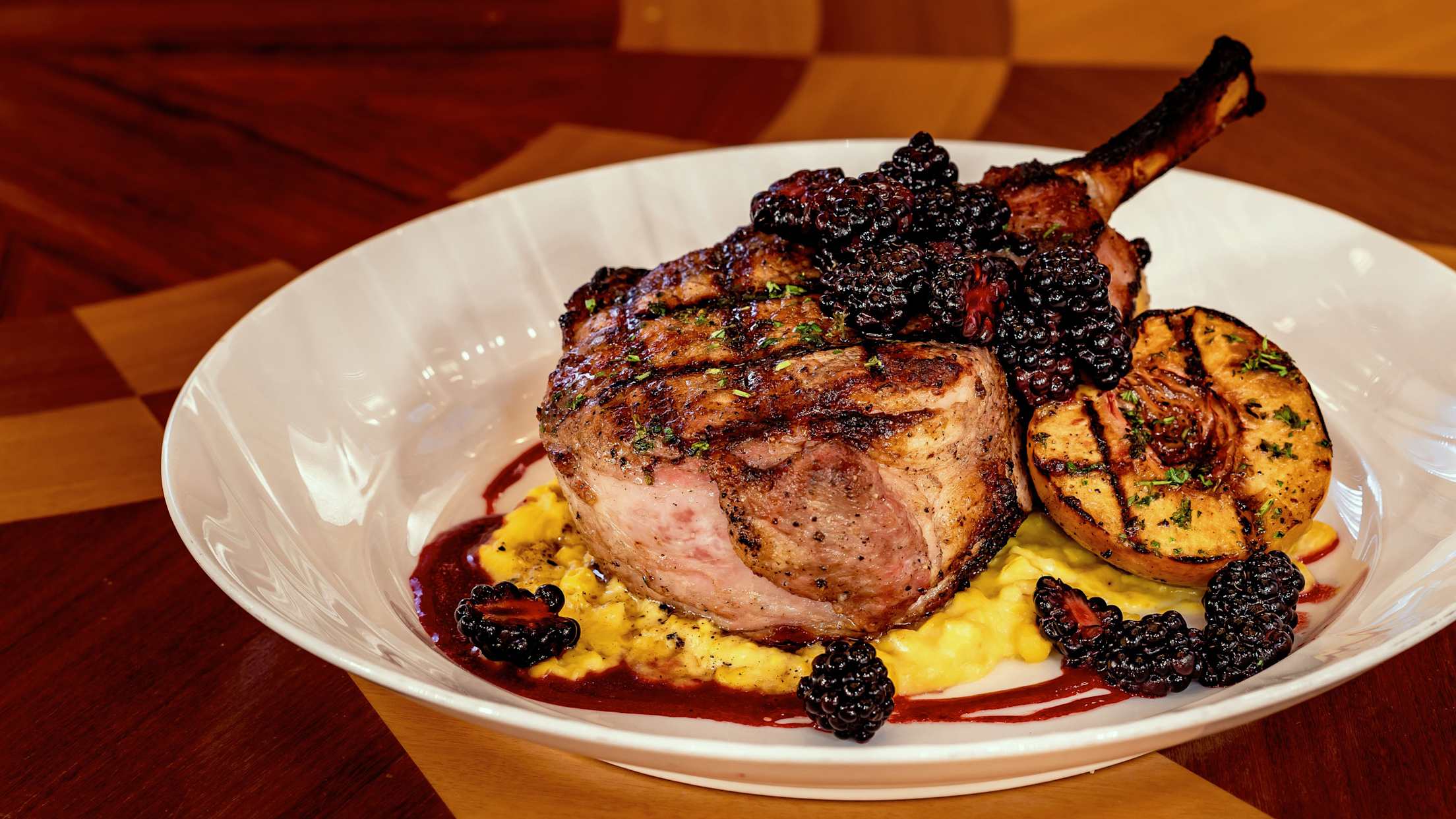 Pork chop with grilled beach and blackberries from Carthay Circle Restaurant on a white plate.
