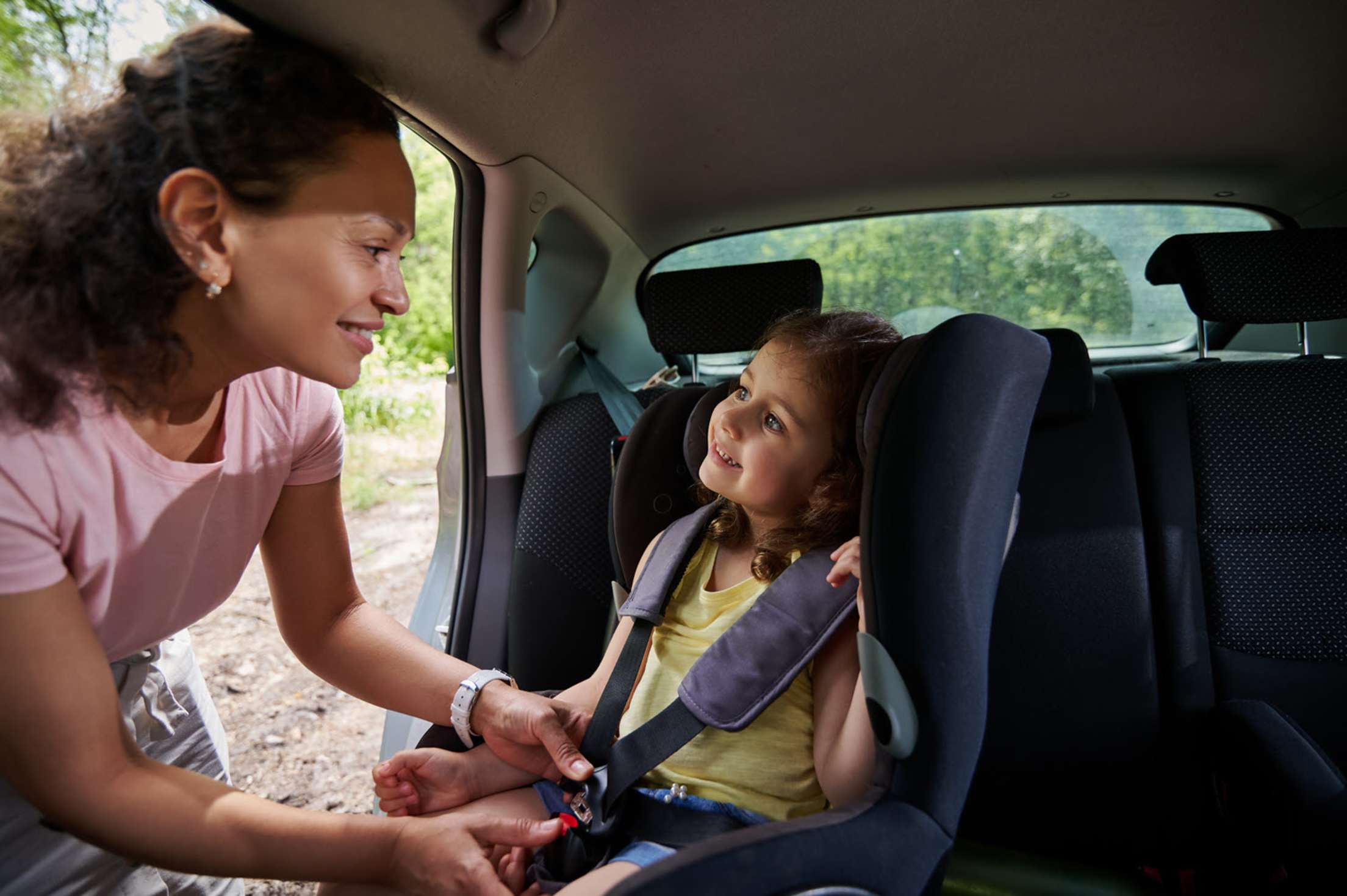 A mom straps her daughter into a car seat.