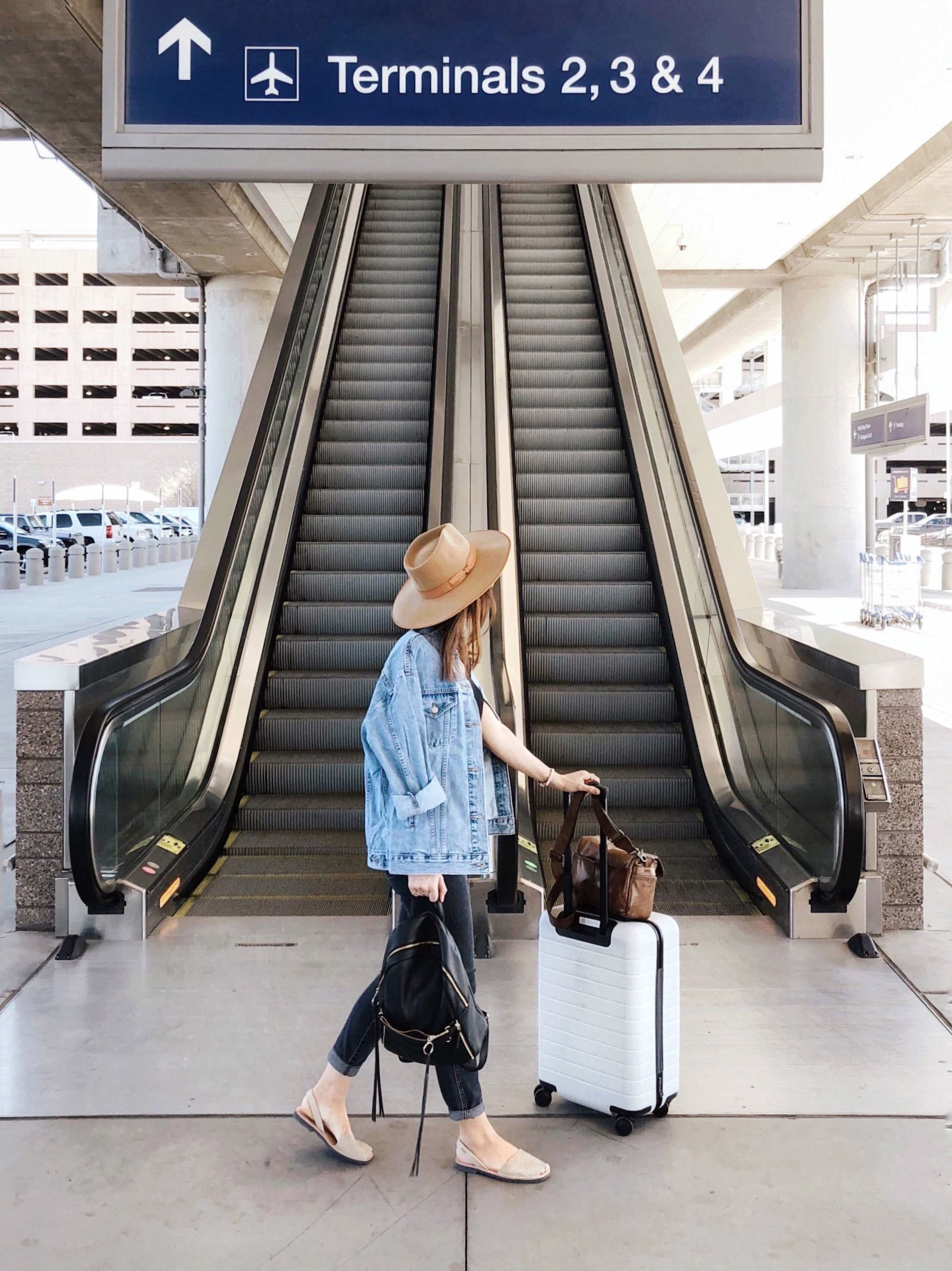 Woman walking to airport terminal with white rolling luggage.