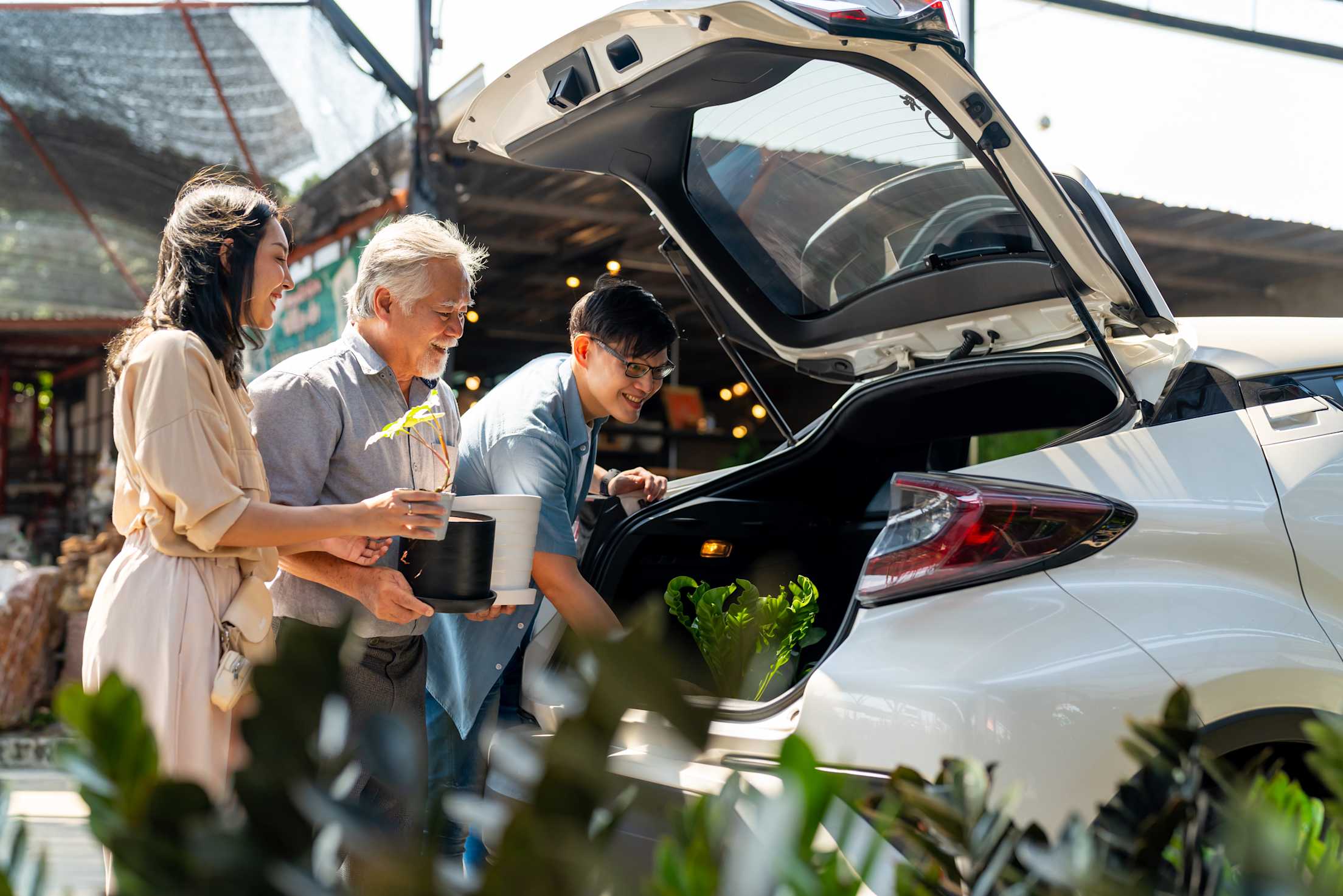A family put new plants into the trunk of their car at a nursery.