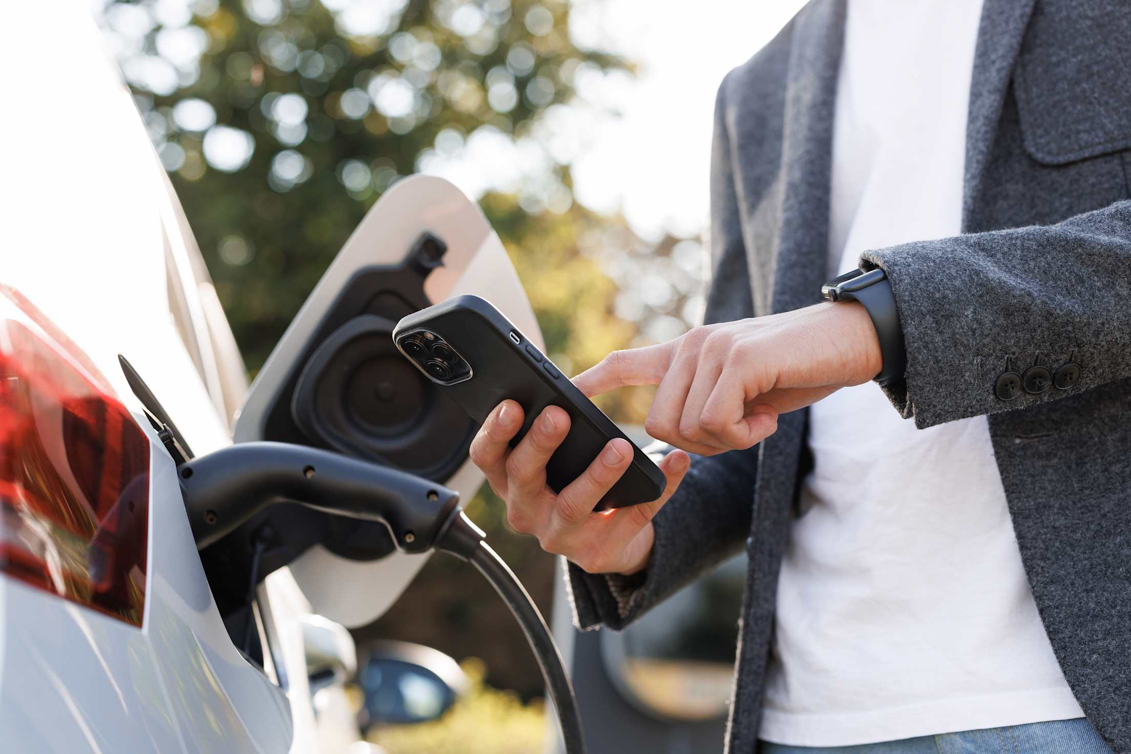 An EV driver looks at the charging app on his phone while at the EV charging station.