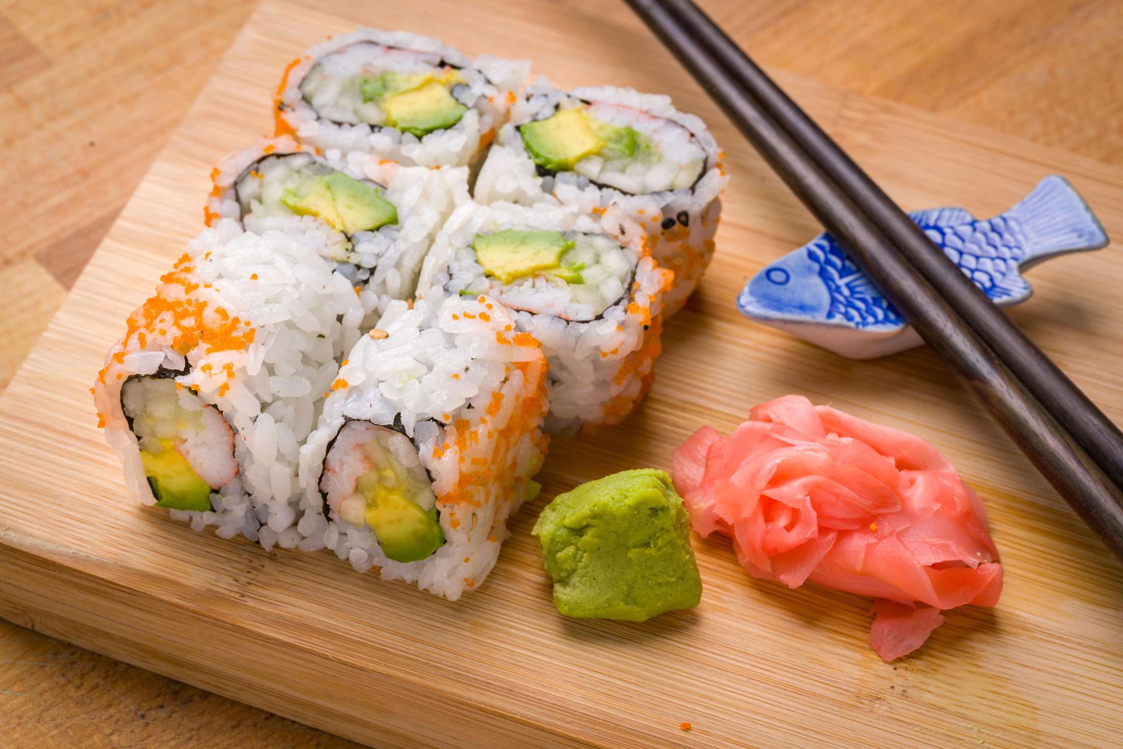Sushi California rolls appetizer with rice, avocado, pickled ginger, and chopsticks.