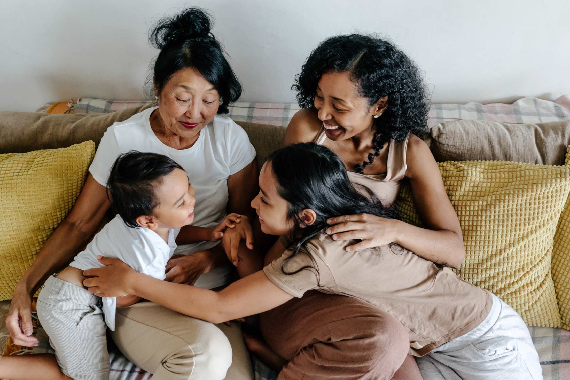 A grandmother, mom, and two kids play together on a couch.