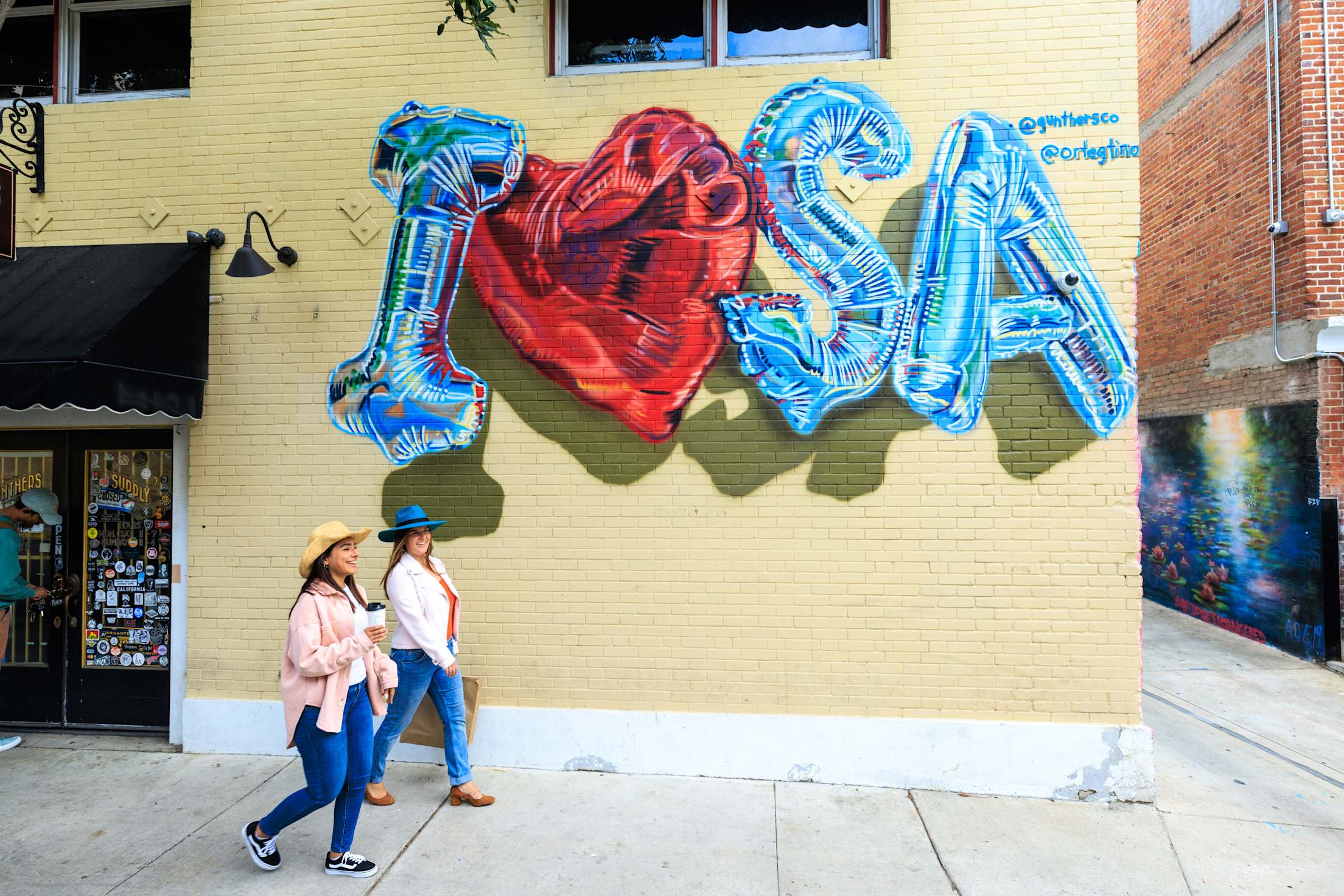 Two women stroll past an "I 'Heart' Santa Ana'" mural.