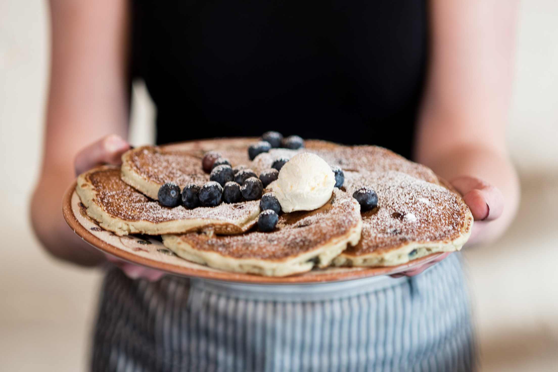 A plate of pancakes topped with blueberries, powered sugar, and butter.