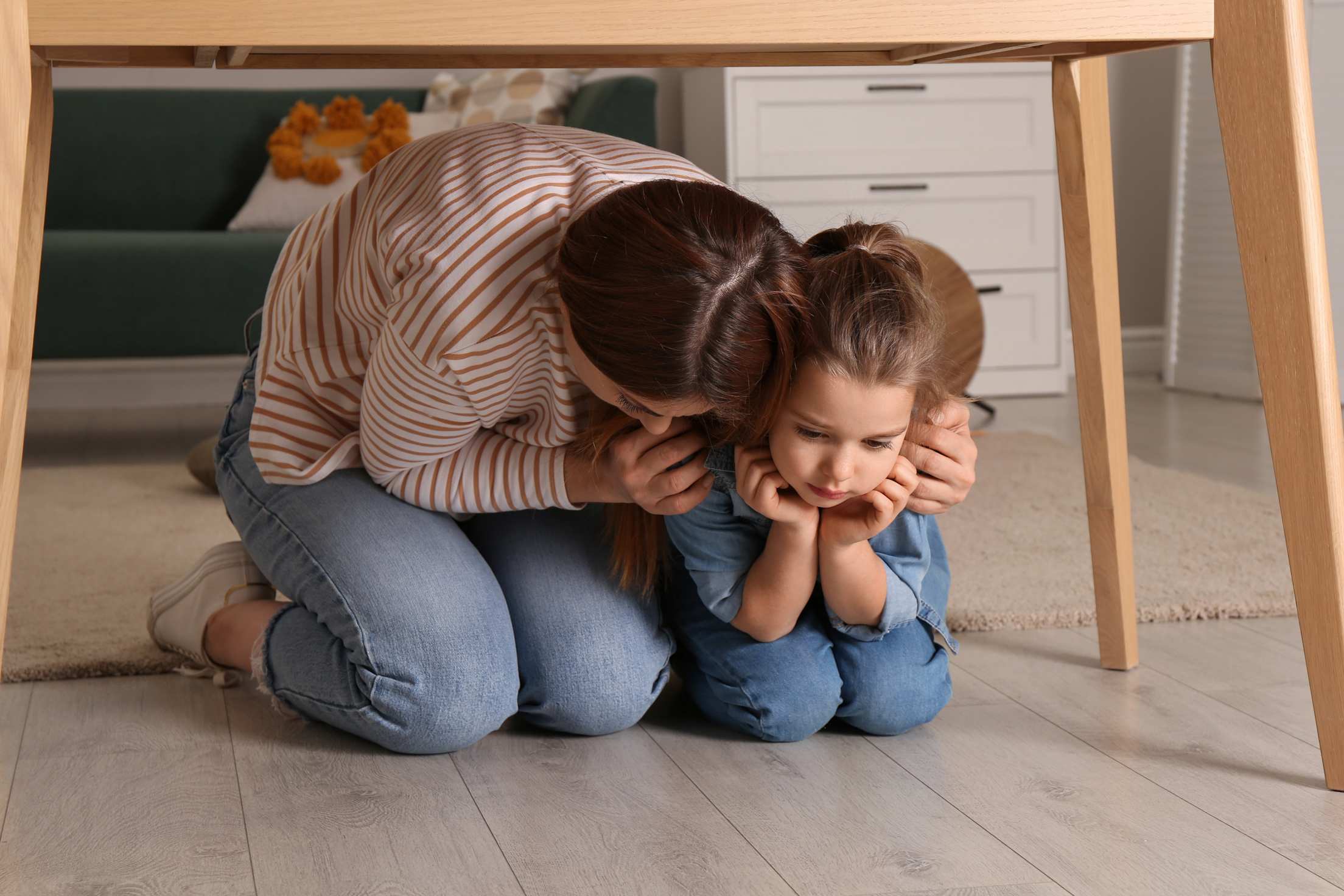 A woman and a young girl crouch under a table during an earthquake.