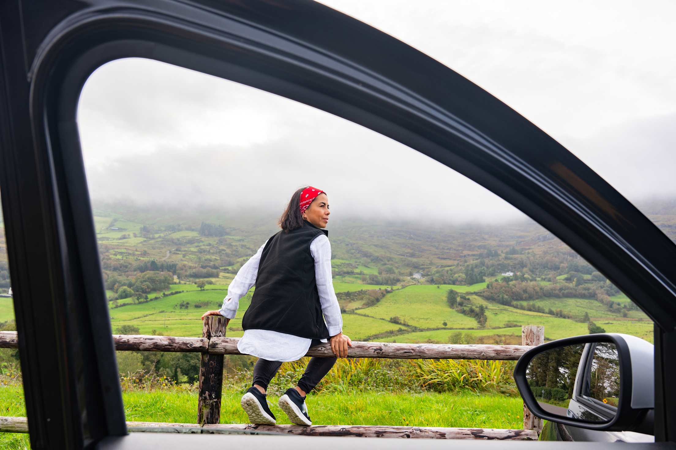 A woman sits on a fence beside her rental car in Spain.