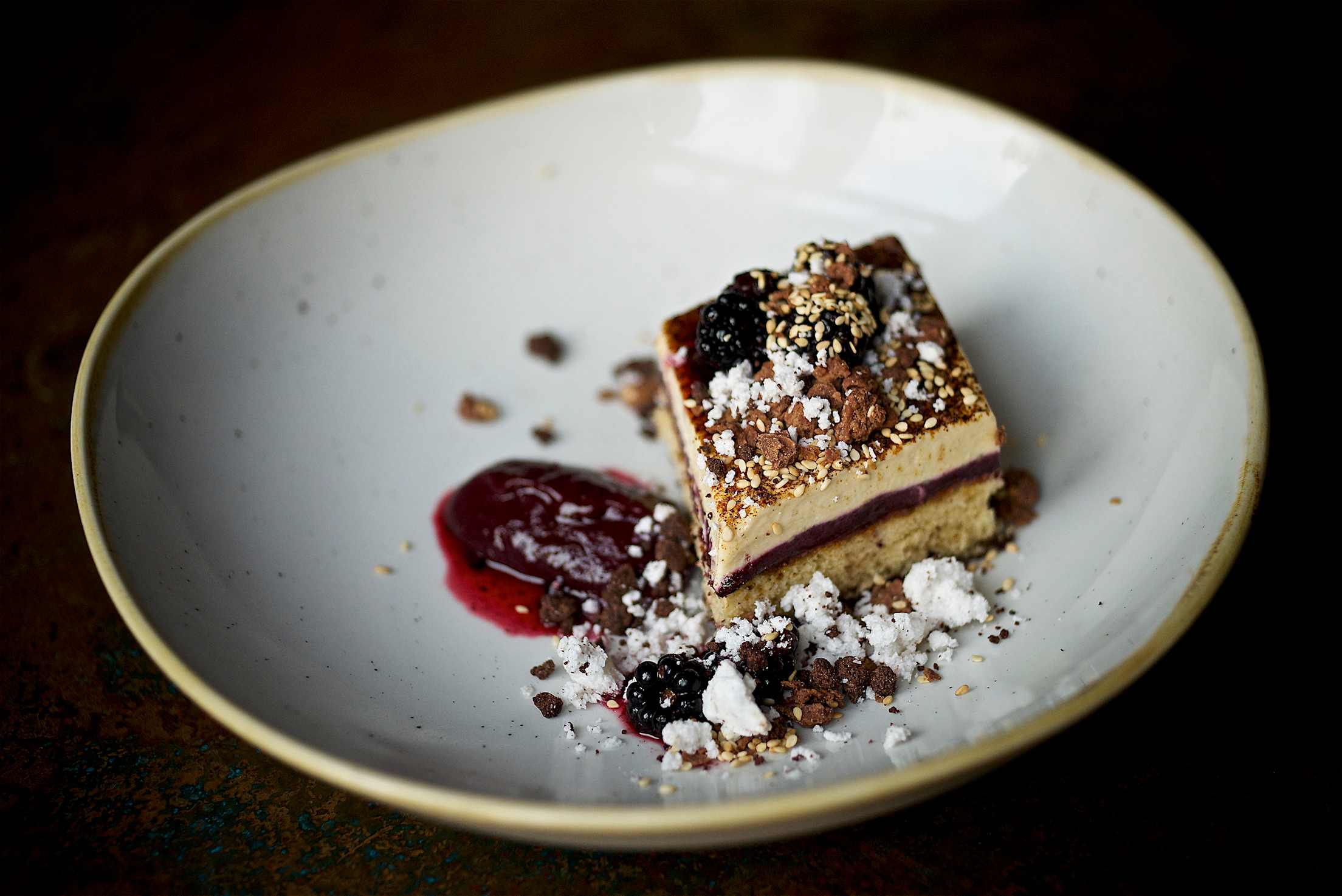 artful dessert, resembling cheesecake or tiramisu, with blackberry sauce, cocoa, coconut, sesame, on a stoneware plate at Le Pigeon in Portland, OR