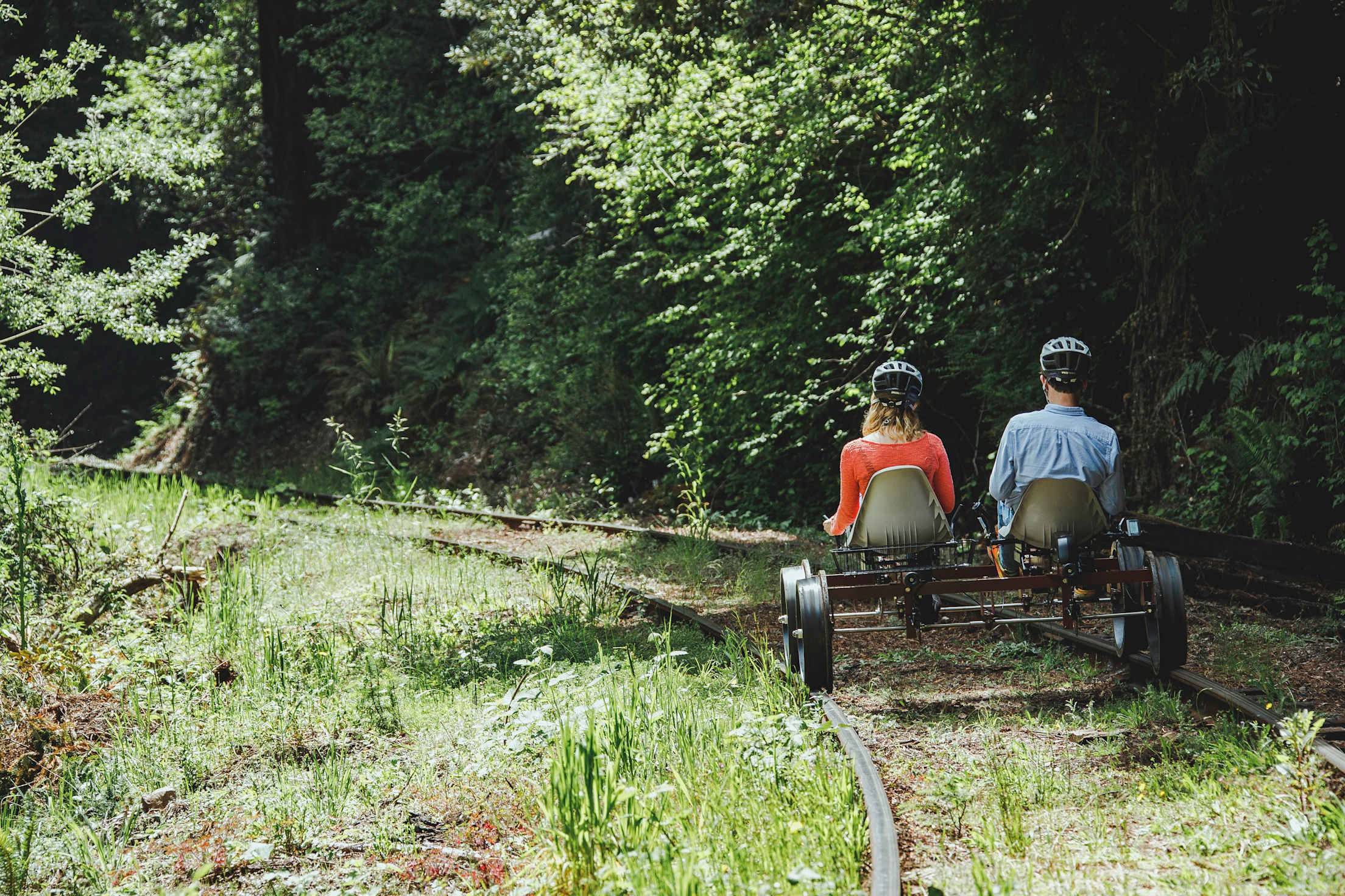 two people pedaling a railbike through the woods are seen from behind