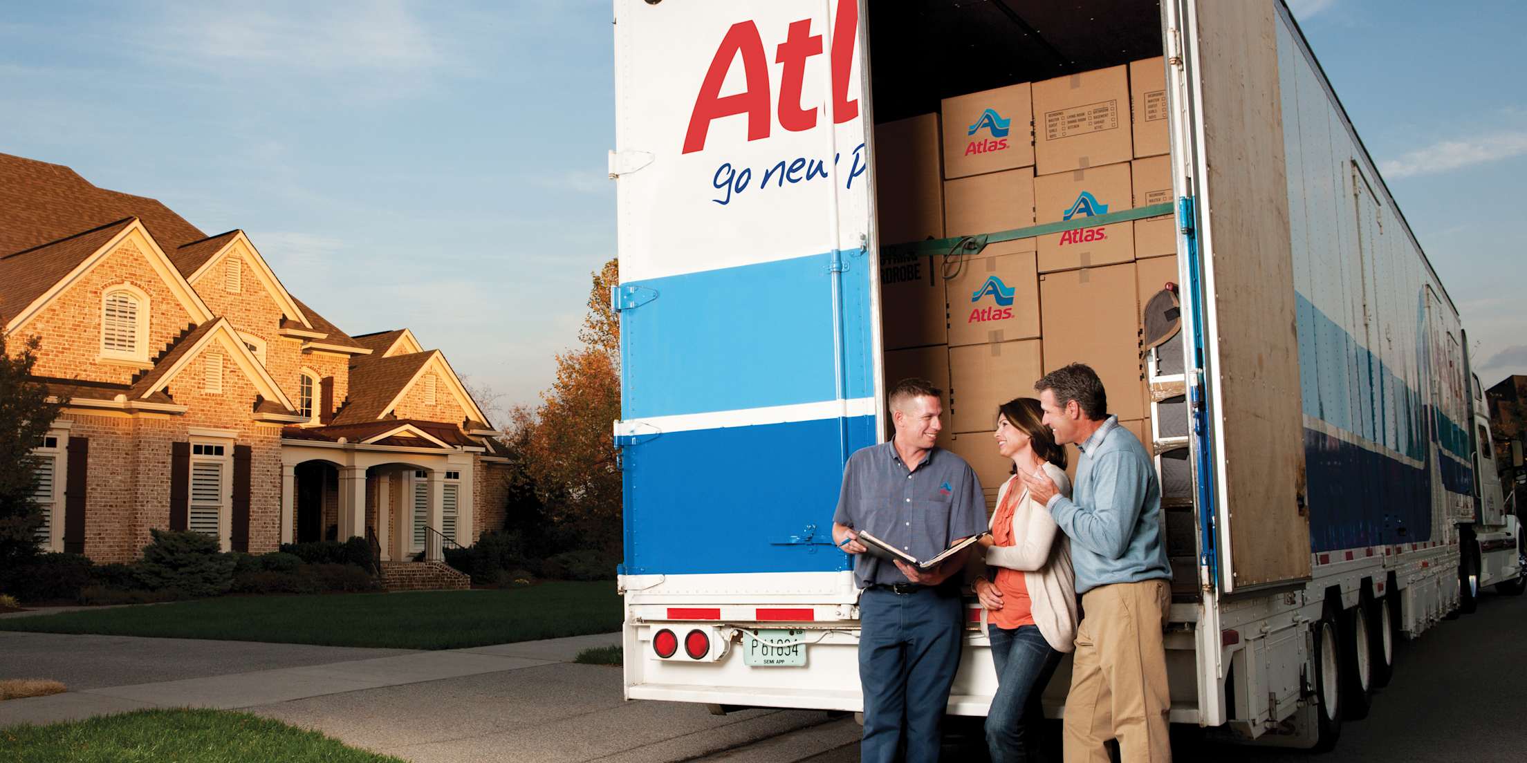A professional mover, a man and a woman stand in front of a moving truck packed with boxes.