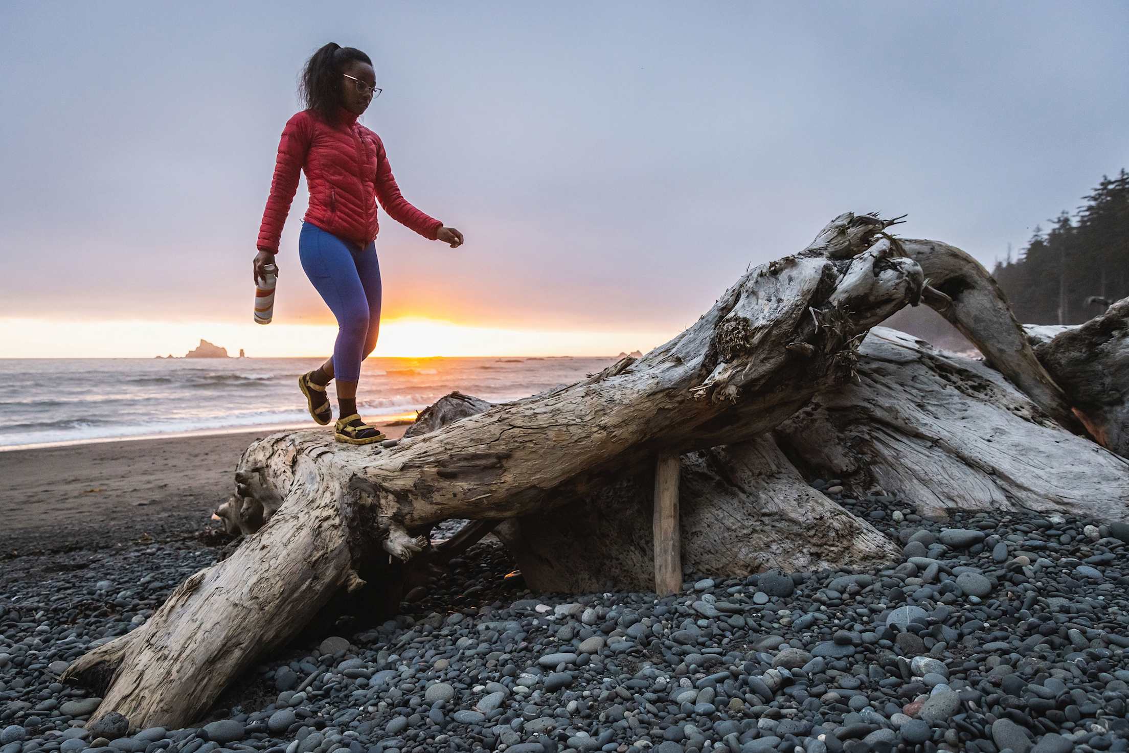 A woman walks on a washed-up log on a beach at Olympic National Park.