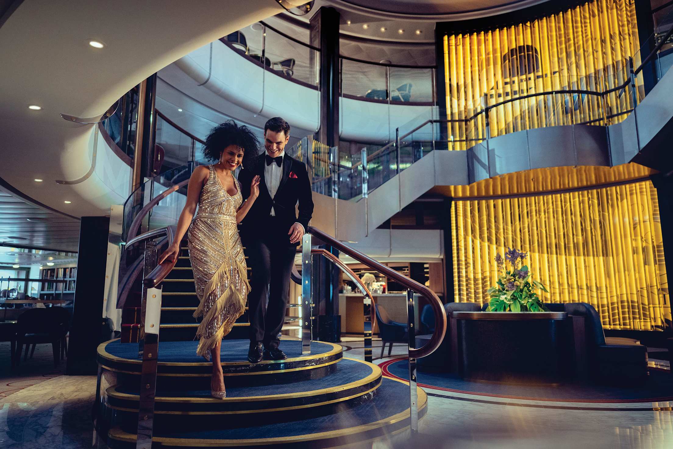 A well-dressed couple descends stairs to grand lobby of the Queen Anne cruise ship.