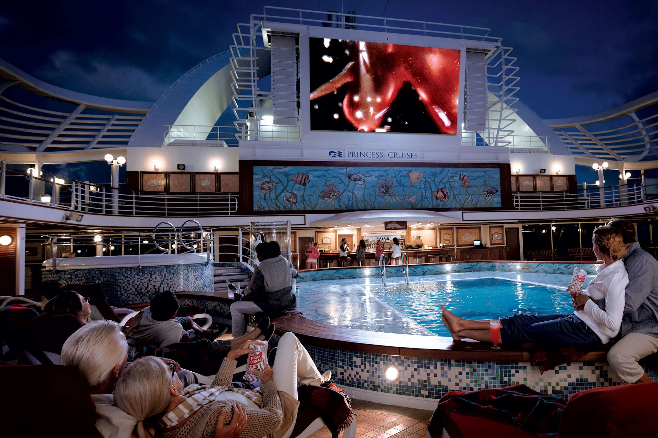 People gather around a cruise ship pool to watch a movie at night.