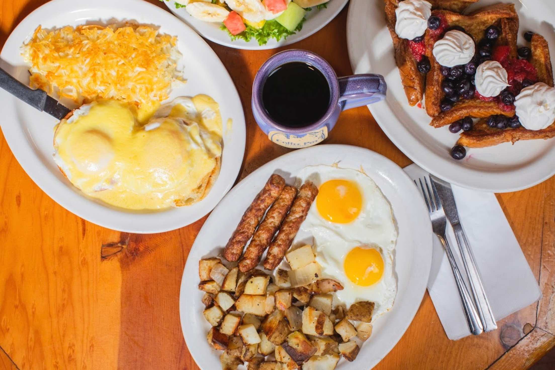 a wooden table with a spread of waffles, eggs, sausagse, hash browns and coffee