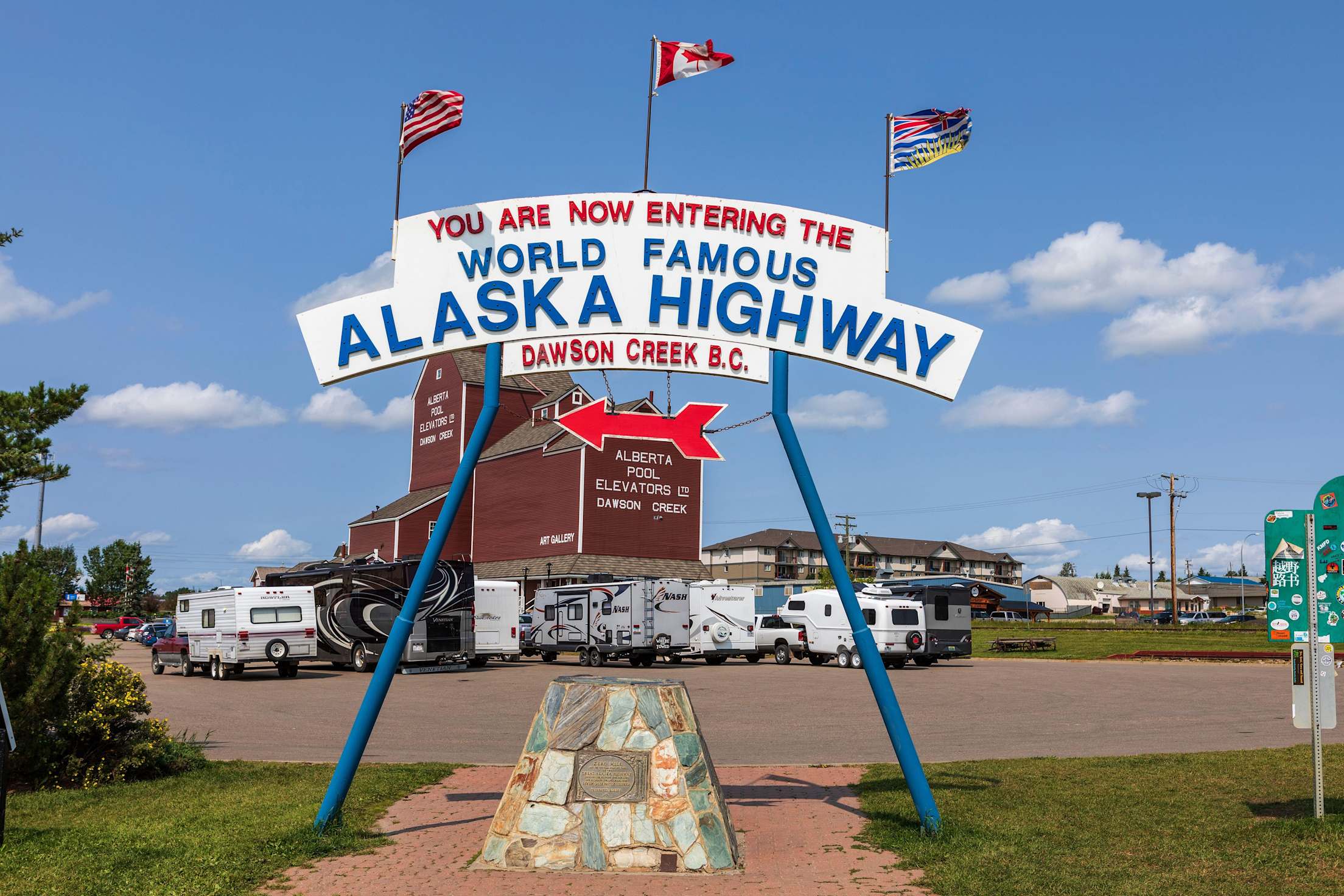 a sign reading 'you are now entering the world famous alaska highway, dawson creek b.c.' with american and canadian flags
