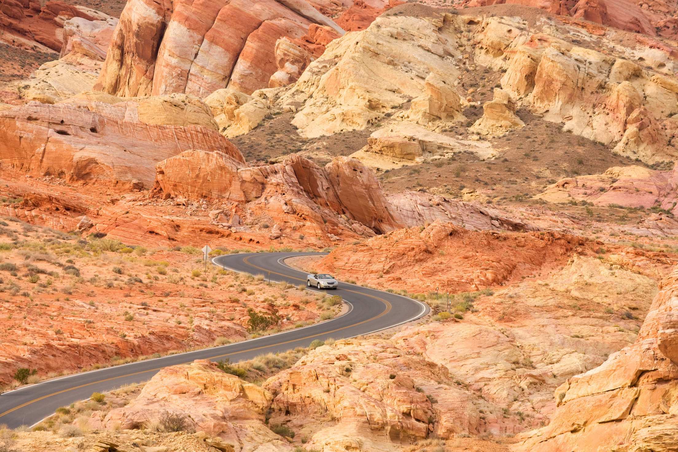 a car winds through a valley of red rocks