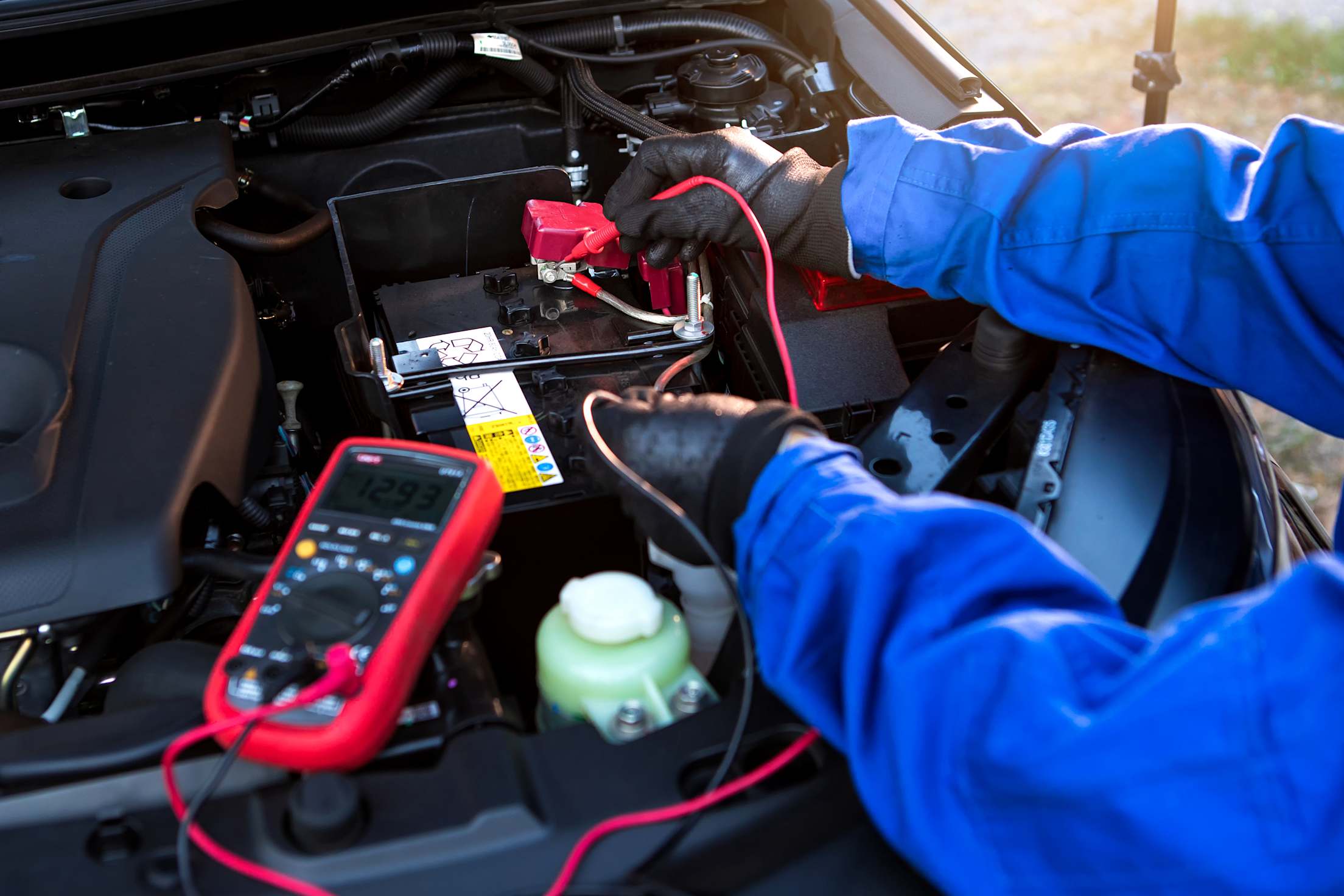 a mechanic checks the voltage of a car battery with a multimeter