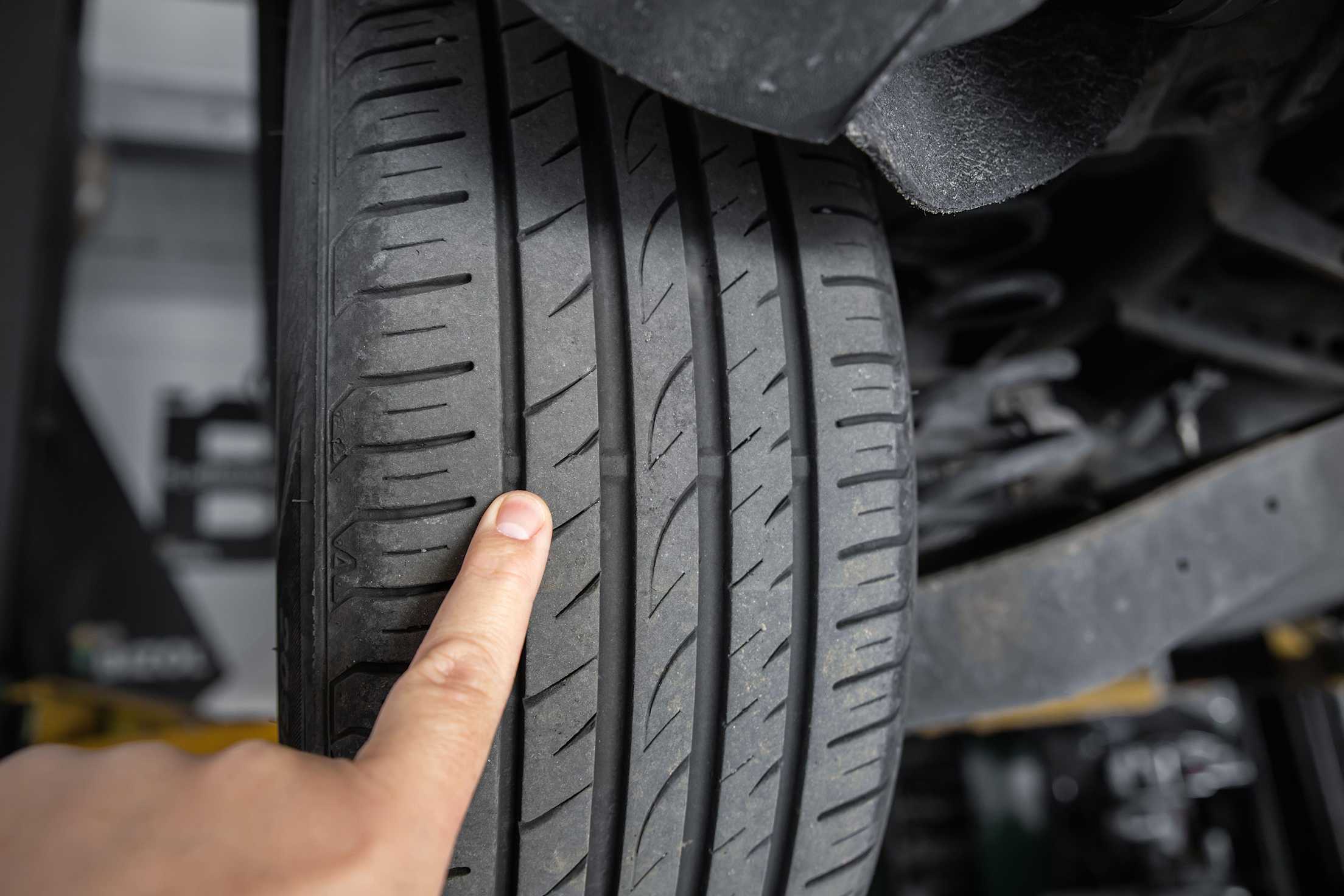 a close-up of tire wear indicators on a tire, with a mechanic pointing them out