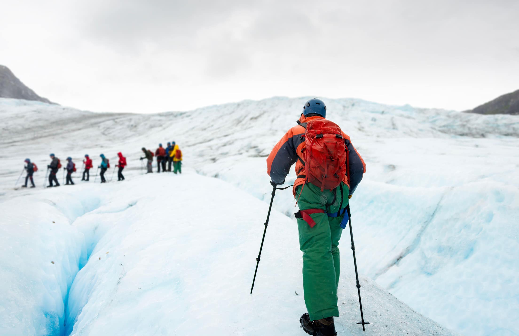 people hike on ice using crampons and walking sticks in Alaska