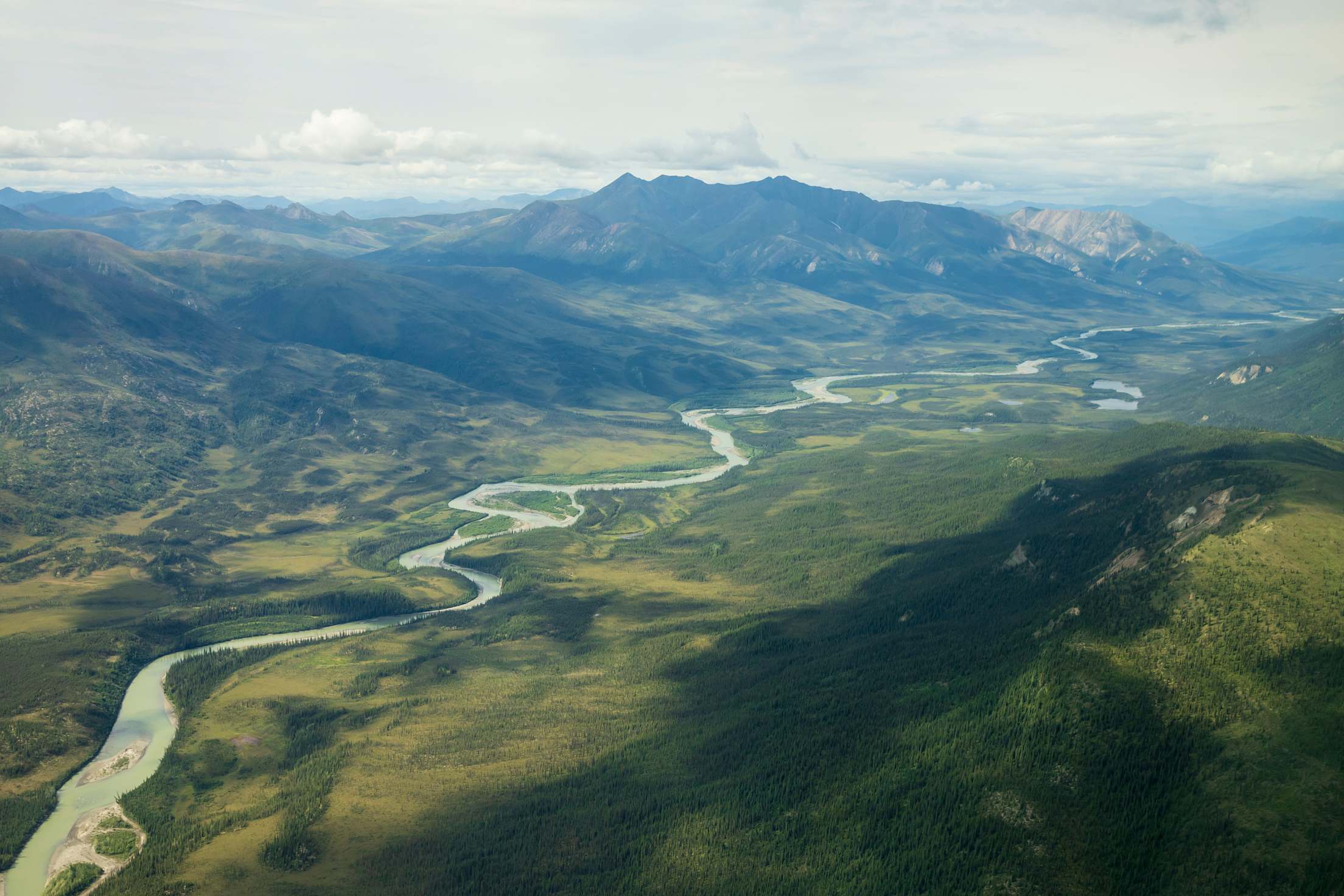 an aerial photo of a river through green valleys and mountains in Alaska