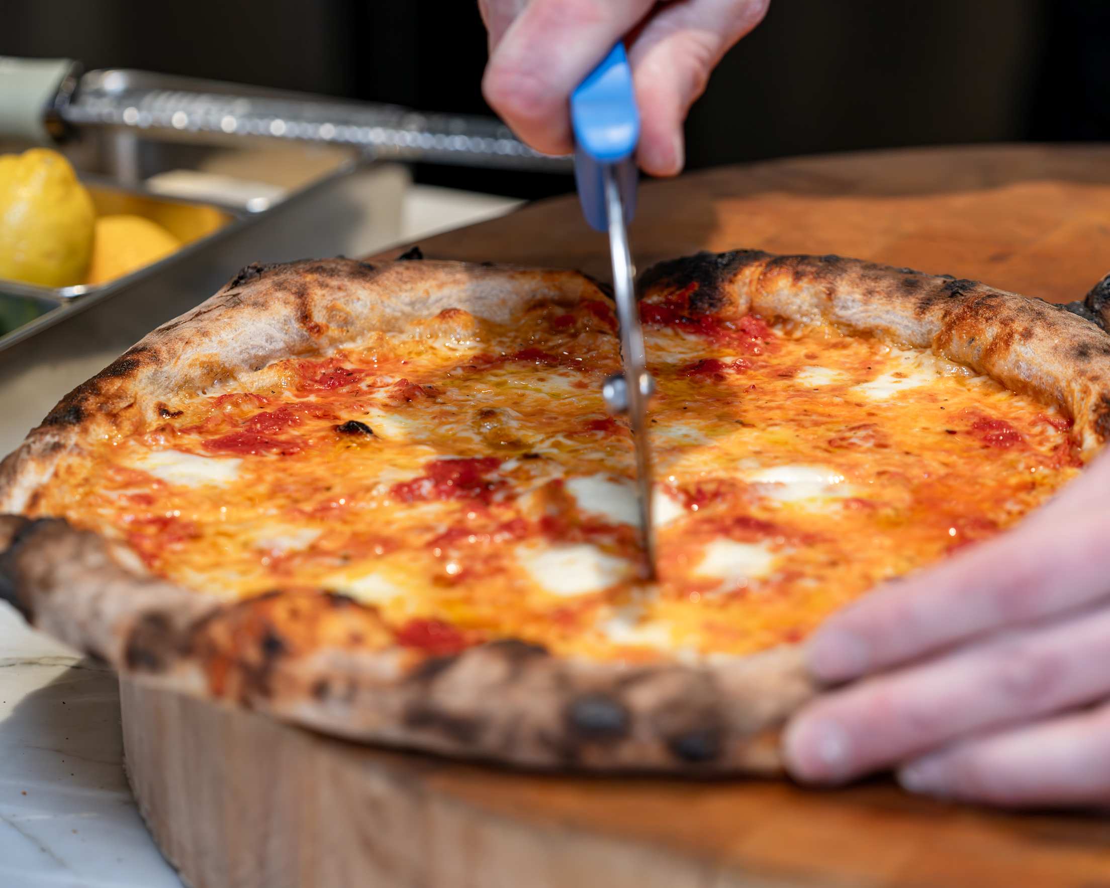 a person slices through cheese pizza