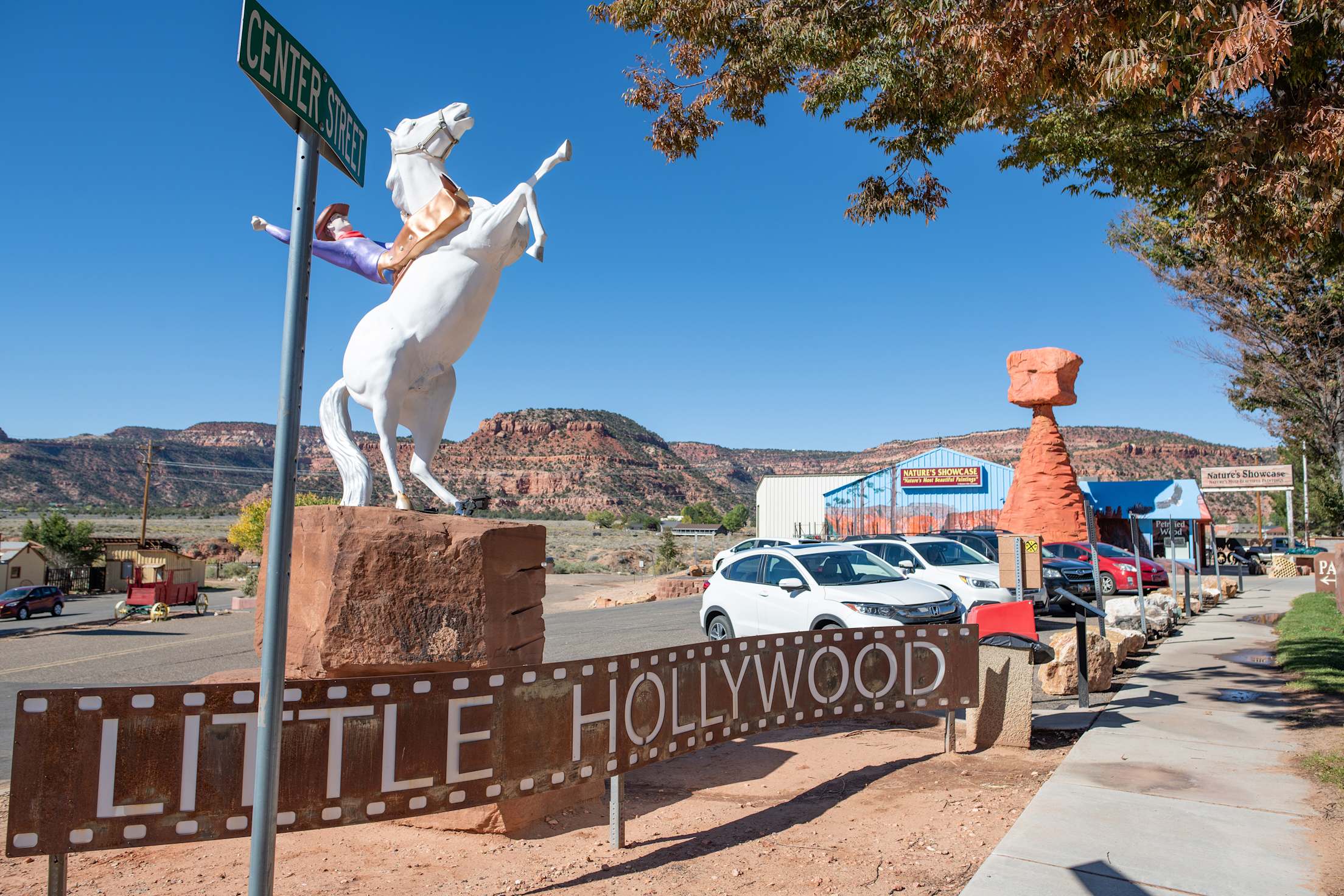 a sign that says 'little hollywood' in front of a parking lot with mountains in the background