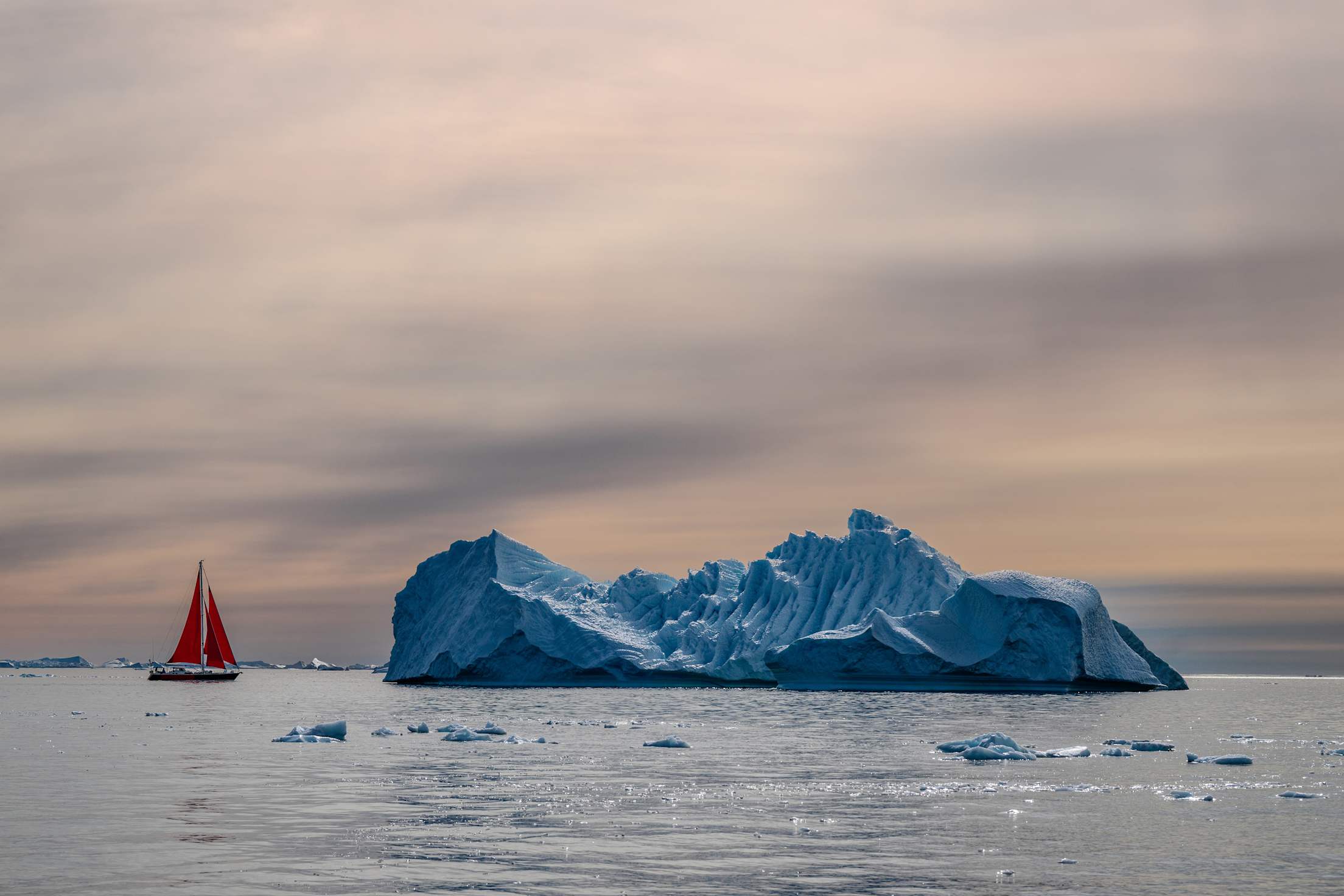 a small iceberg next to a red sailboat