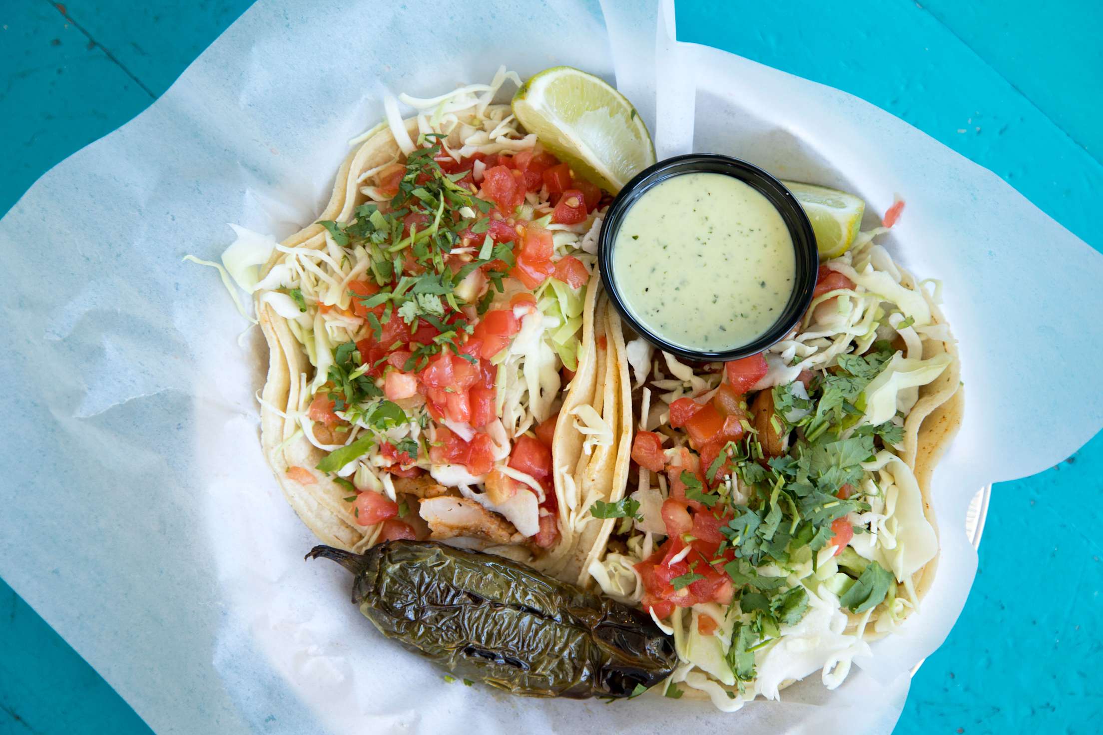 A plate with two fish tacos topped with slaw, with a charred poblano and sauce on the side.