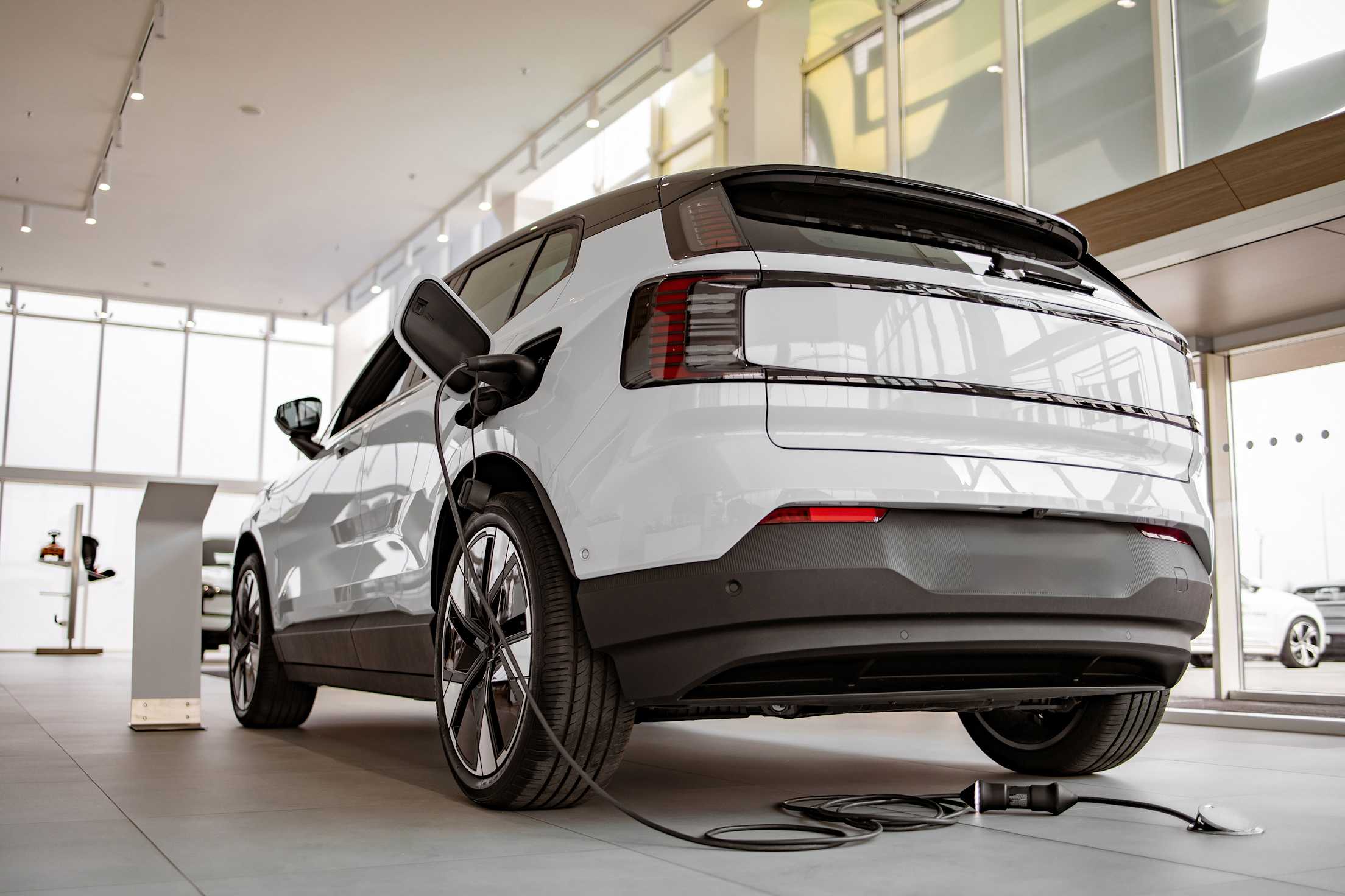 A white EV SUV charges in a dealership showroom