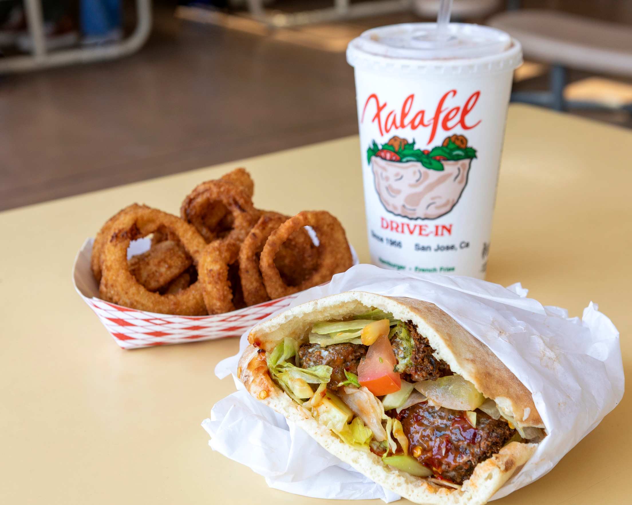 a falafel in pita with onion rings and a drink