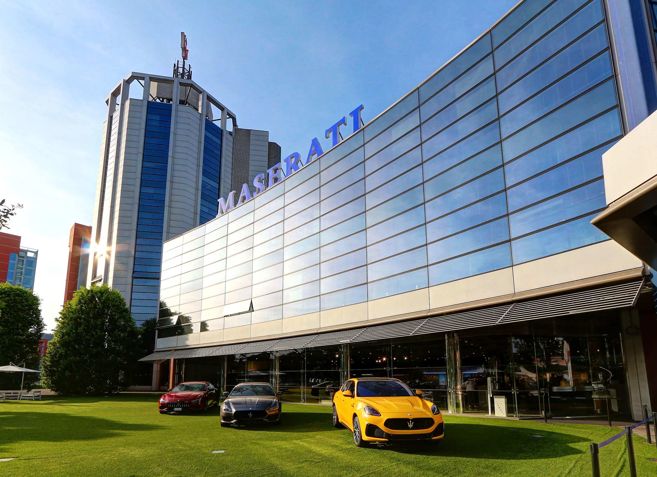 Three Maserati sports cars outside a glass block office building and showroom at the Maserati factory.